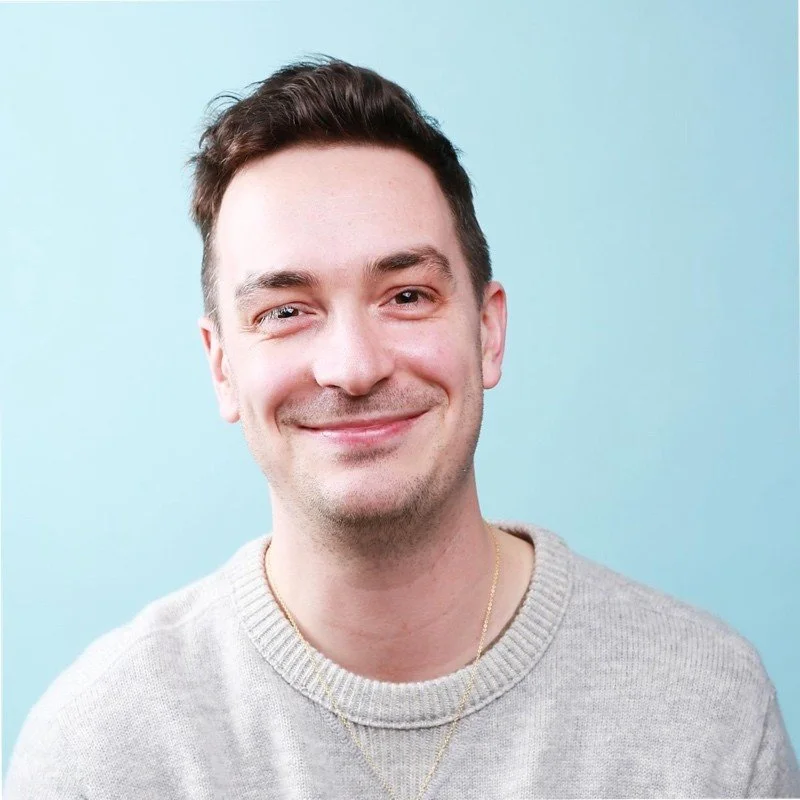 Smiling person in a grey sweater against a blue background.
