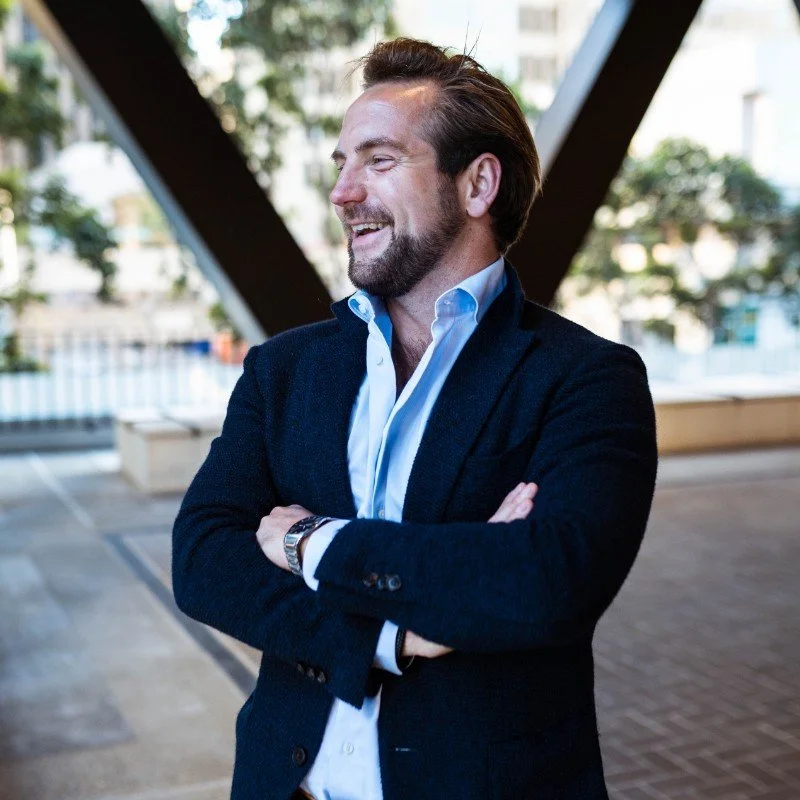 Smiling man in a suit standing outside with arms crossed