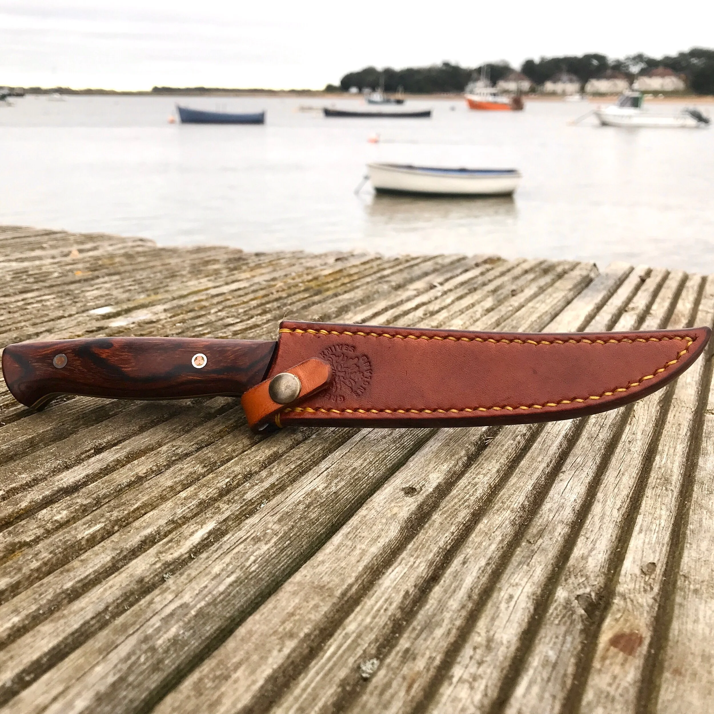 A fishermans filleting knife in its leather belt sheath hand made in the UK by Green Man Knives