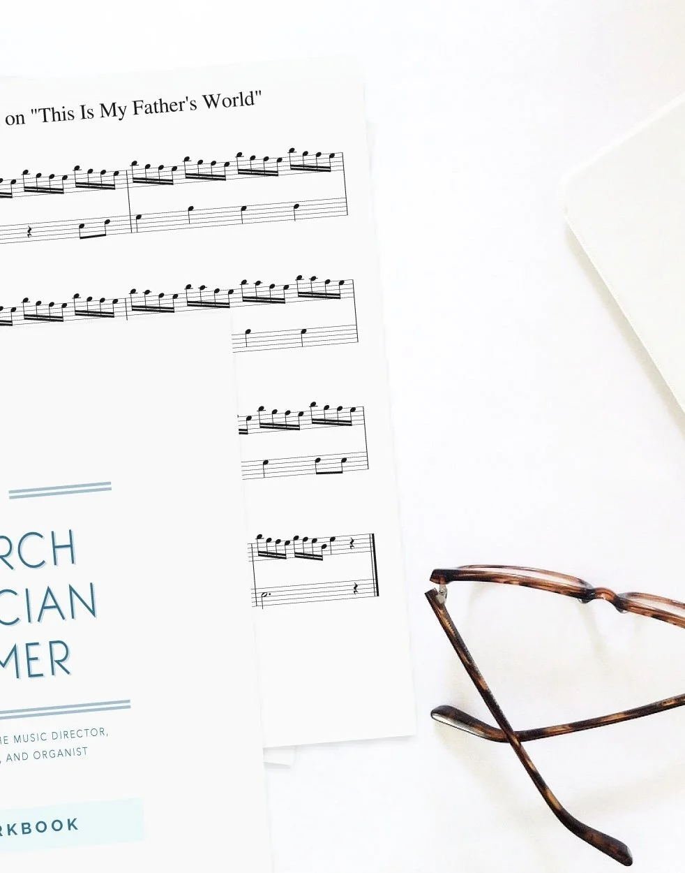 The Church Musician Primer workbook and sheet music with glasses on a white desk