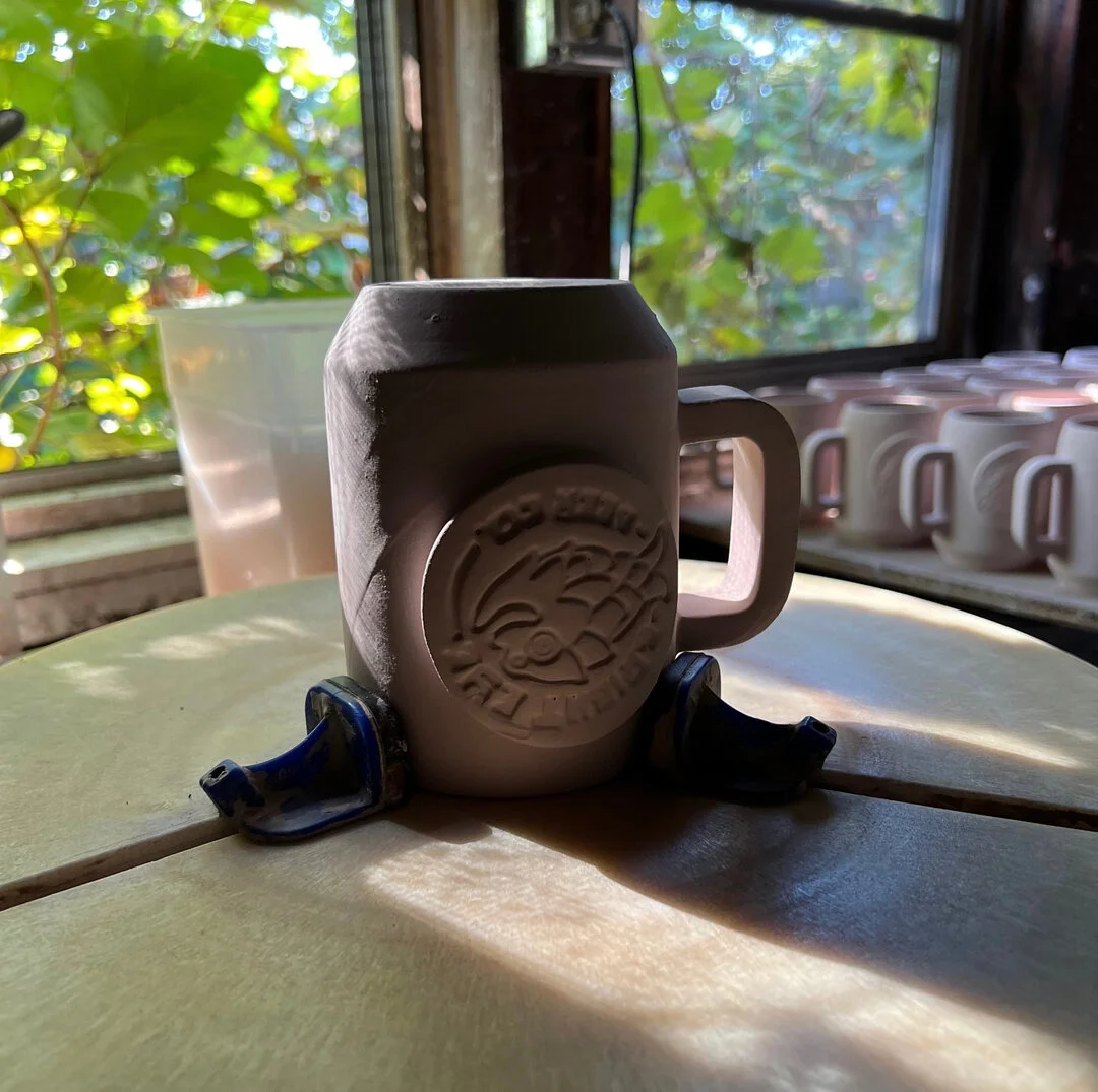 Cleaning off glaze from the logos on these mugs before their final firing in the kiln.