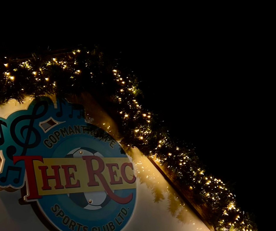 Decorative Christmas garland with lights above a sign for 'The Rec' sports club in a dark setting.