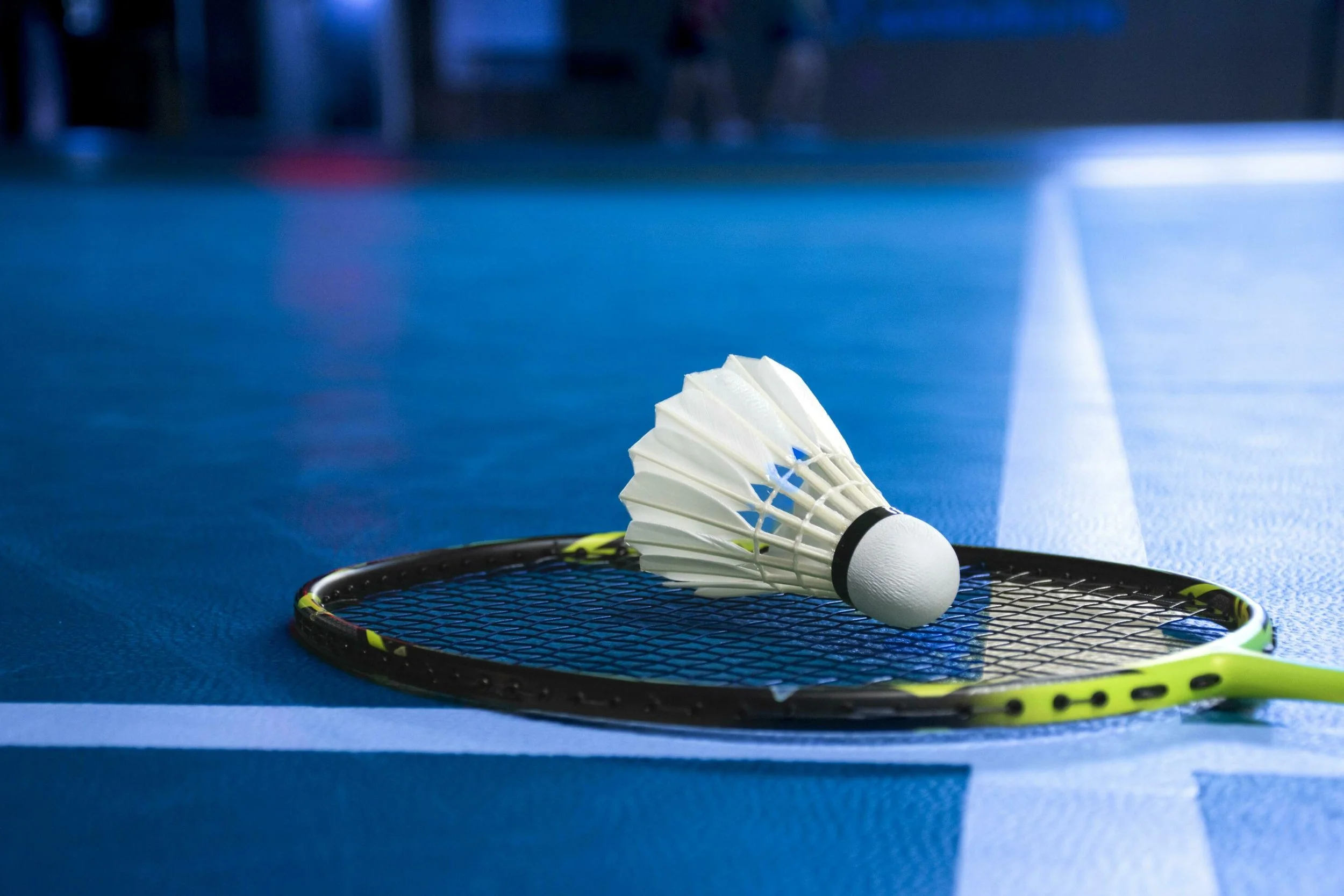 A badminton racket lying on the court with a badminton shuttlecock placed on it.