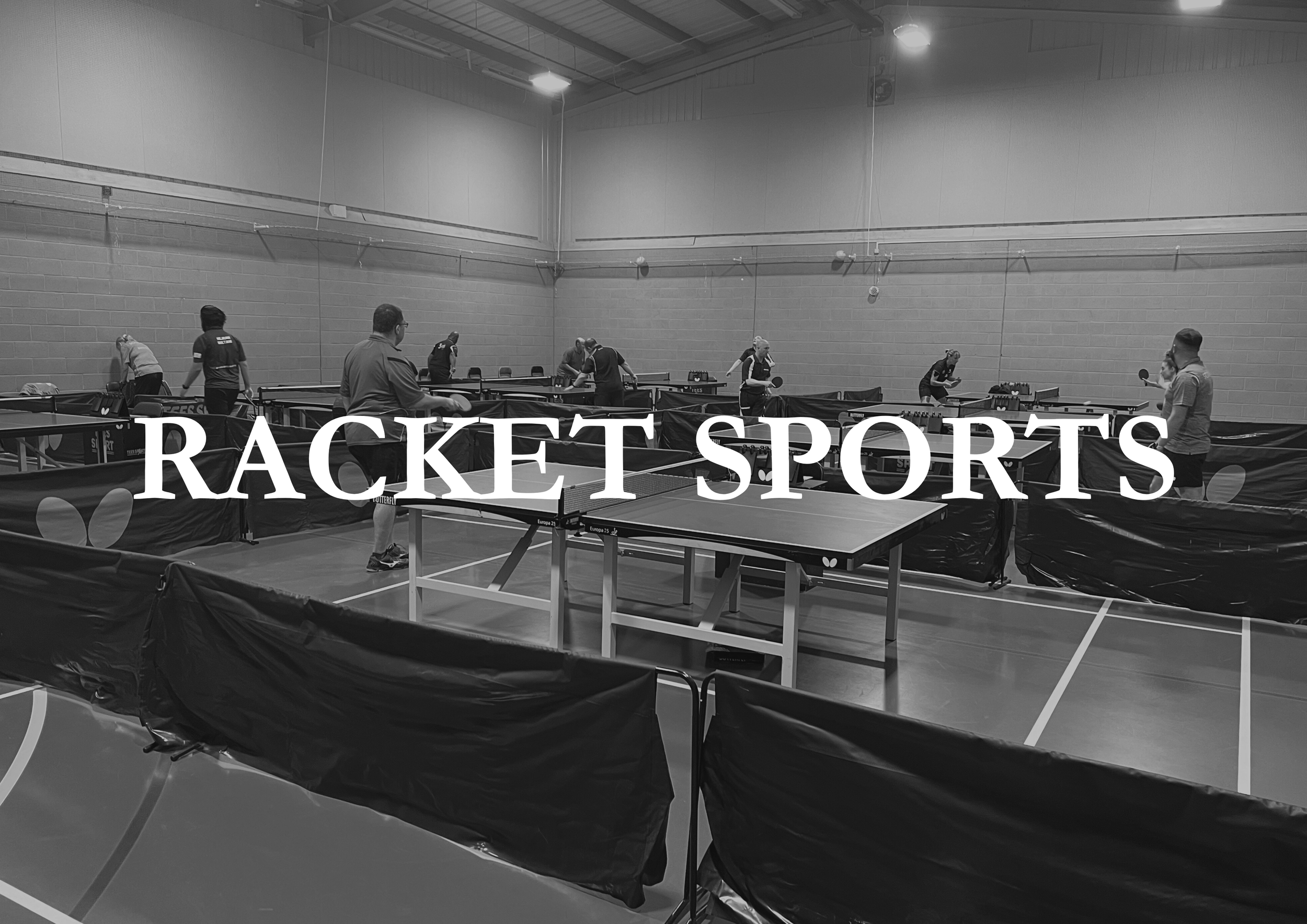Black and white photo of a table tennis training session in an indoor gym, with several players practicing and a large banner with the words 'RACKET SPORTS' overlaid.