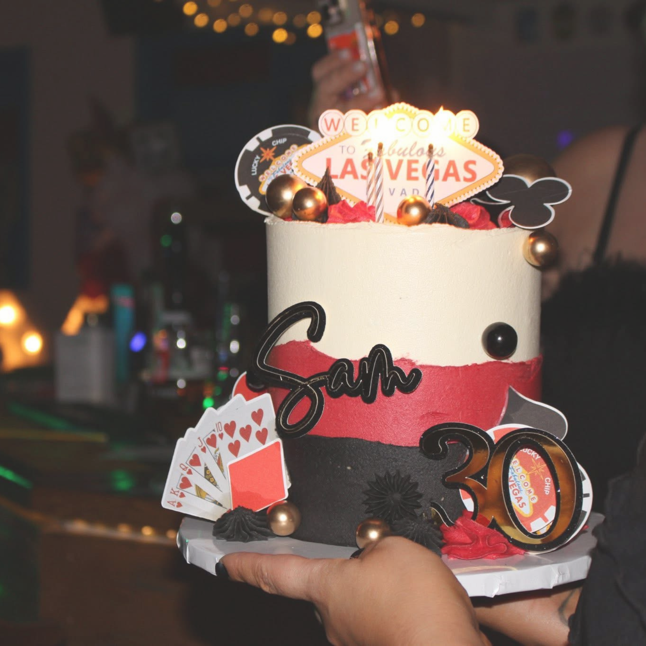 A decorated birthday cake with a Las Vegas theme, featuring a white and black color scheme, gold and black spherical accents, playing cards, and a casino sign topper celebrating a 30th birthday.