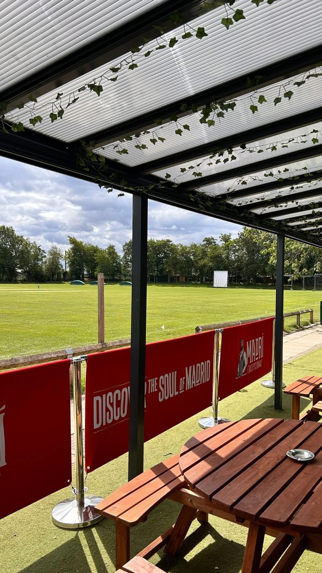 View from a covered outdoor area overlooking a grassy field with banners that read "Discover the Soul of Madrid."