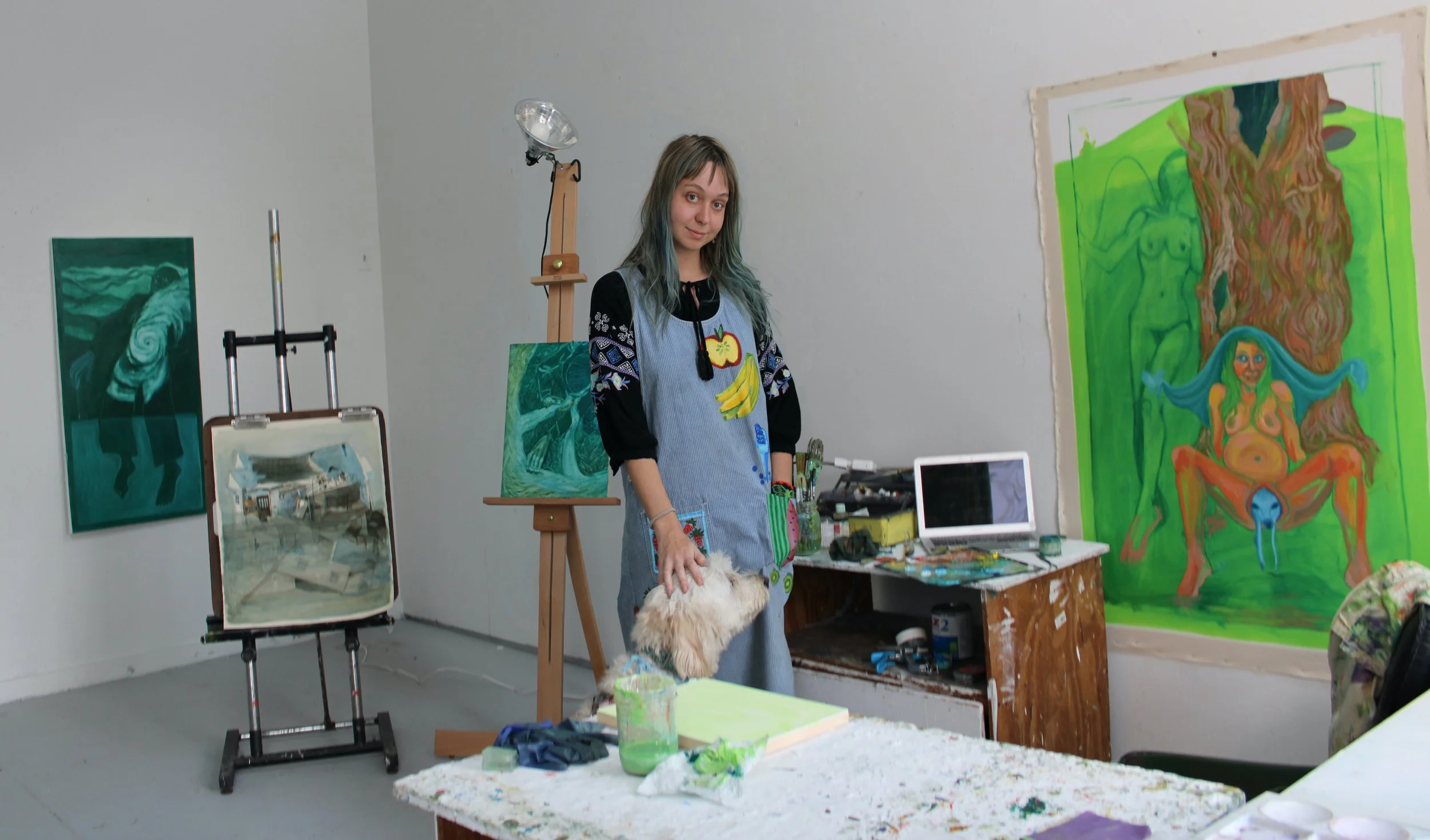 studio photo from vermont studio center, artist stands in a handpainted fruit dress with four paintings around them