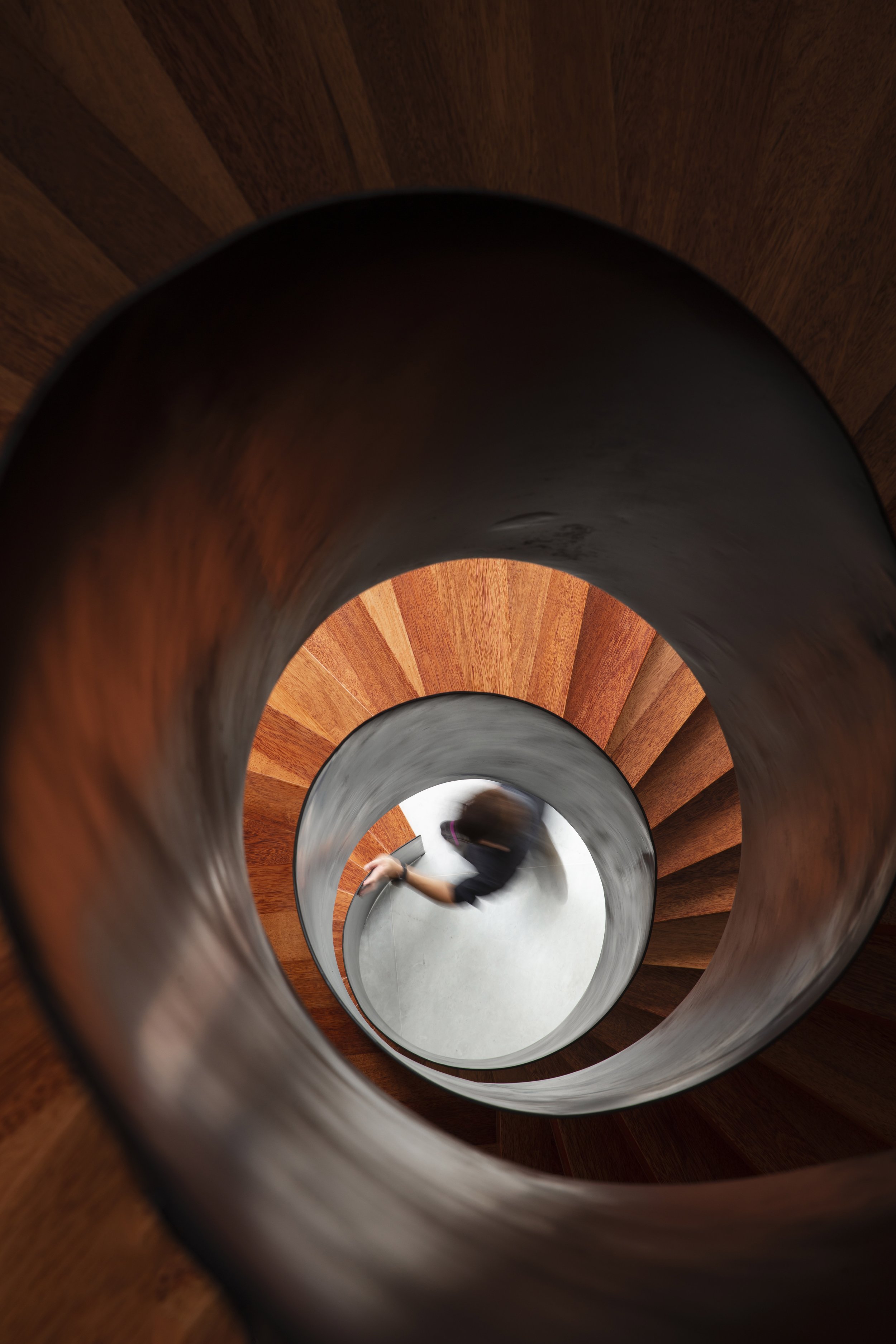Looking down a spiral wooden staircase with a person walking at the bottom.