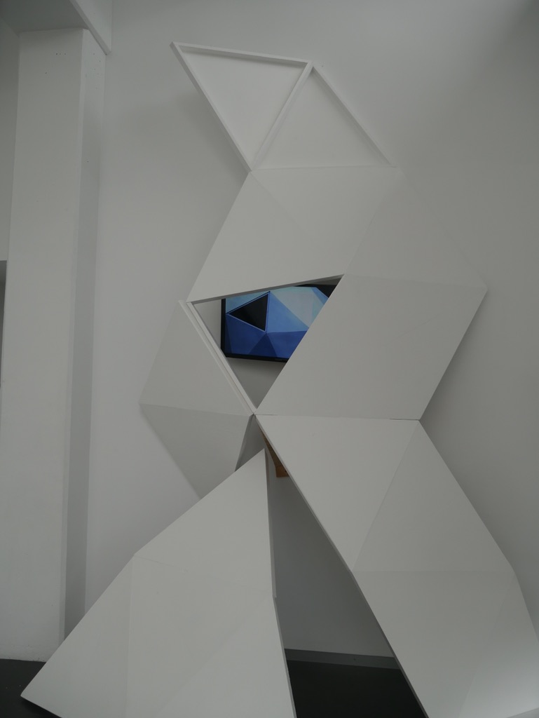 Over the past several years Rebecca Pilcher has been exploring the manifold implications of the Town Belt, surrounding Wellington as both a highly constructed, controlled, and manipulated area, and a pastoral, green, and meditative space ripe for creative and discursive play. In the current installation, Pilcher has reconfigured some portions of a timber geodesic dome that she exhibited in two radically different settings in 2015, once in a public park and once in a gallery space. In the Engine Room, the dome is deconstructed, splayed apart and becomes simultaneously a fractal-like relief and a viewing station, an area in which Pilcher’s videos which appear to have a dreamlike, eccentric quality of their own are, in effect, transmitted through yet another mediating structure, accenting the embodied quality of our positioning as spectators. This provides an intriguing counterpoint to the almost ethereal quality of the footage, figures walking in a reverie, costumed with numerous colourful accessories, offering up an imaginative amalgam recalling both the experimental cinema of Maya Deren and SciFi otherworldliness. By interrupting such footage with * * inter-titles drawn from mindfulness texts, and adding a soundtrack of ambient music, Pilcher gives us a generous glimpse into a conjured space that’s ultimately just as imaginary, constructed, and seemingly elusive as the town belt itself. Martin Patrick Excerpt from Exhibition Catalogue, Is it the Beginning of a New Age. July 2016. http://theengineroom.org.nz/projects/is-it-the-beginning-of-a-new-age