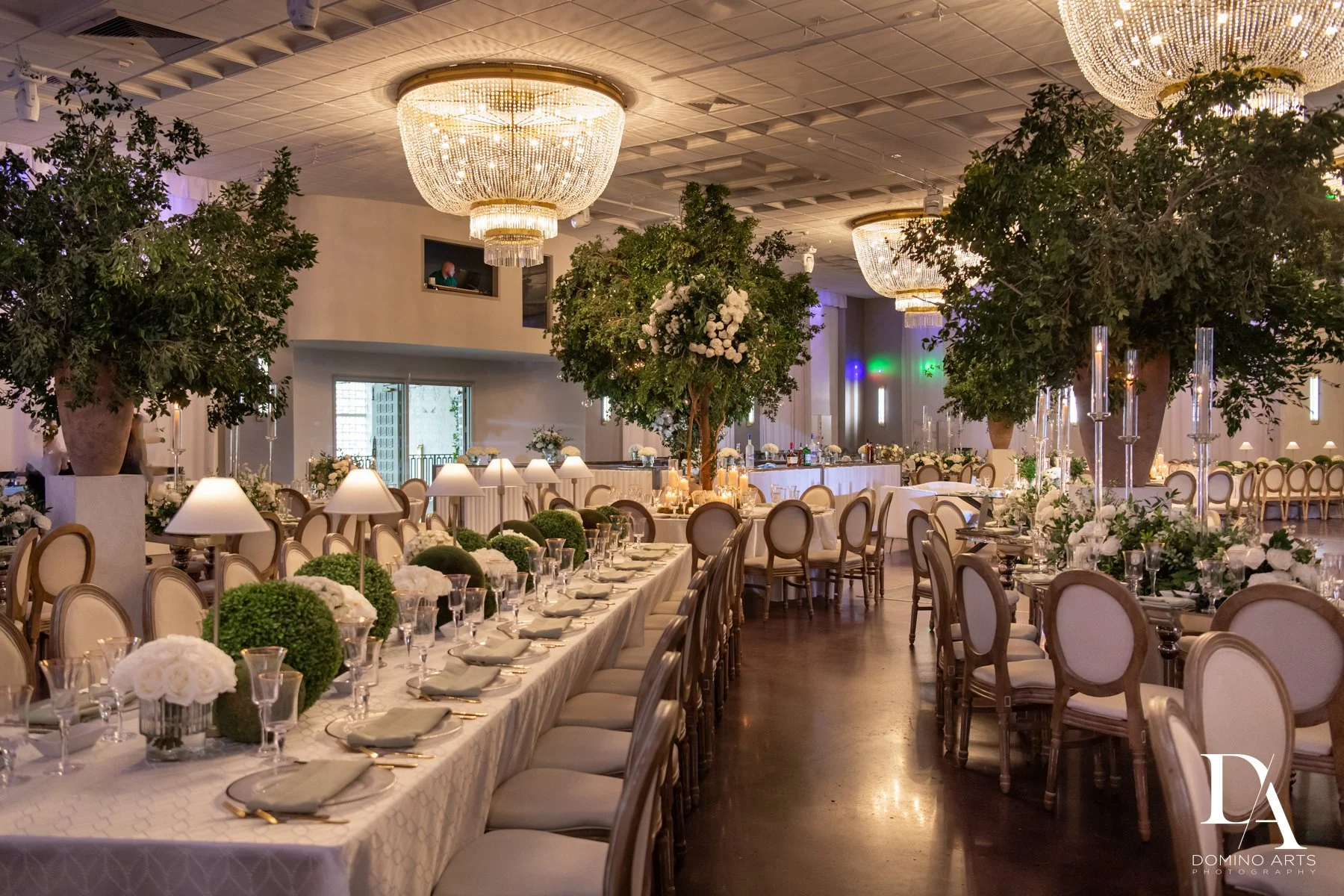 Towering greenery and floral installations transforming the ballroom of Emanuel Luxury Venue into a garden wedding setting.