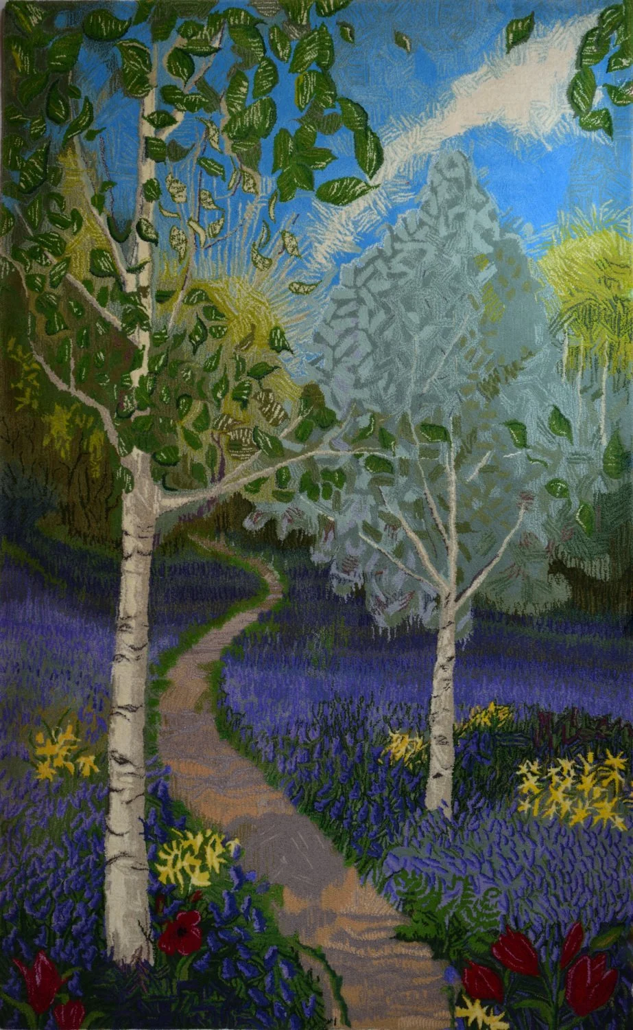 A colorful hand tufted wall hanging of a winding path through a lush bluebell wood, daffodils, and two birch trees with green leaves. There are mountains and a blue sky in the background.