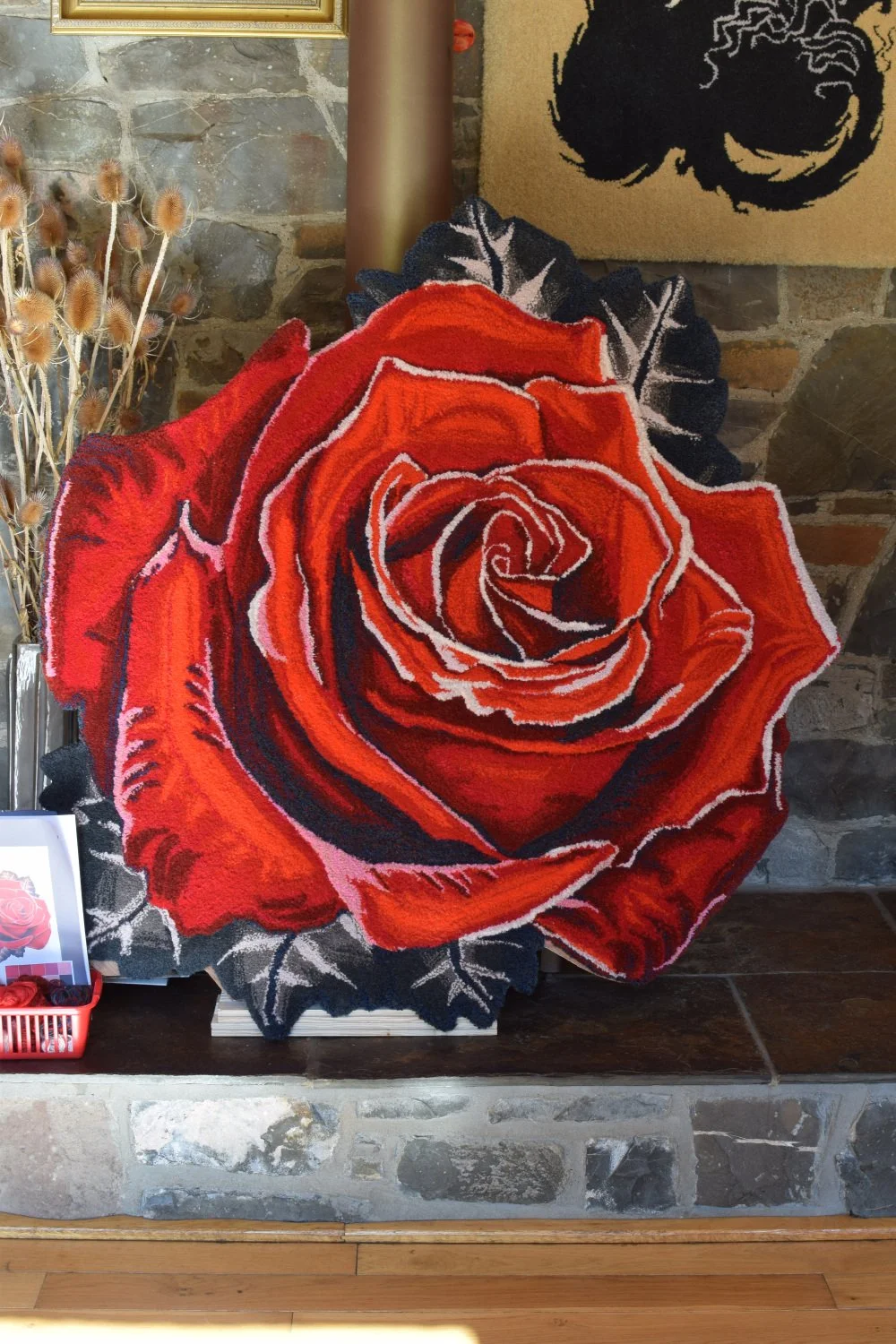 A large decorative rug in the shape of a red rose with intricate petal details, positioned against a brick and stone background.