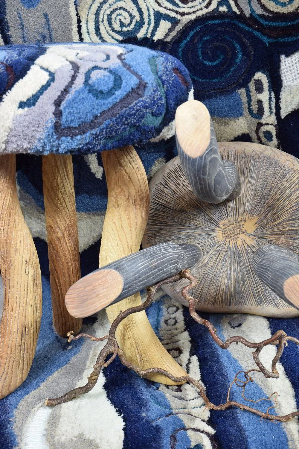 Collection of decorative objects including wooden sculptures, a large rock, and a twisted branch, arranged on a patterned blue and beige rug.