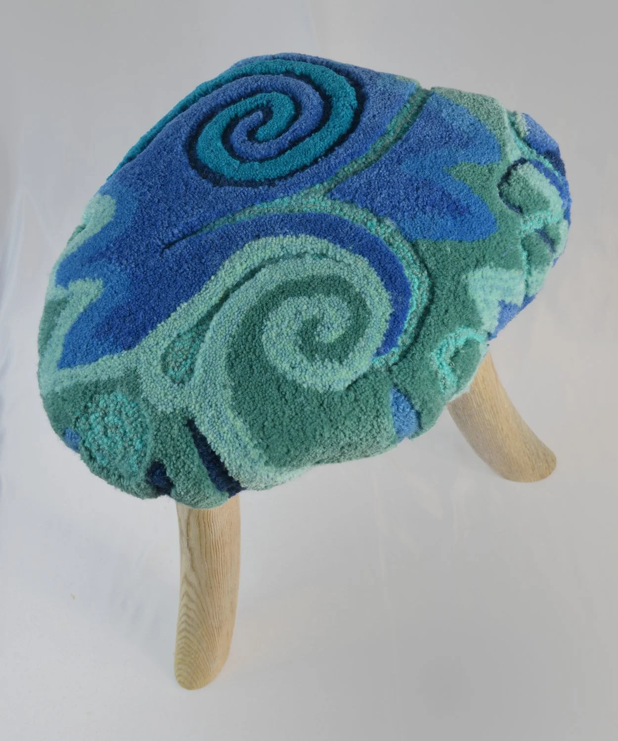 Colorful plush hardwood stool with a swirling pattern of blue and green hues, supported by three wooden legs.