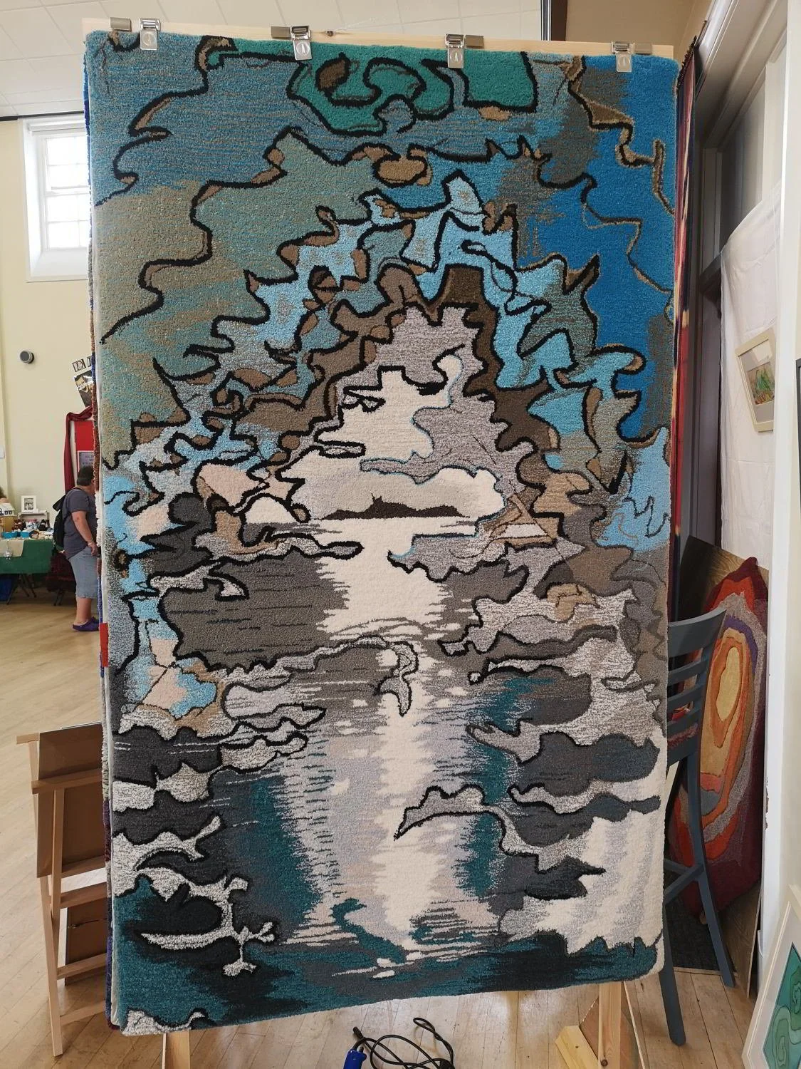 A rug depicting a nature scene with trees and a body of water, with reflections of trees in the water.