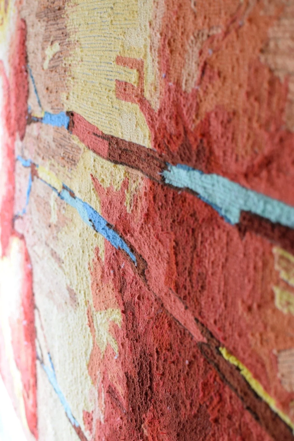 Close-up view of the back of a wool pile textile with colorful tufted abstract design, primarily in shades of red, yellow, and blue.