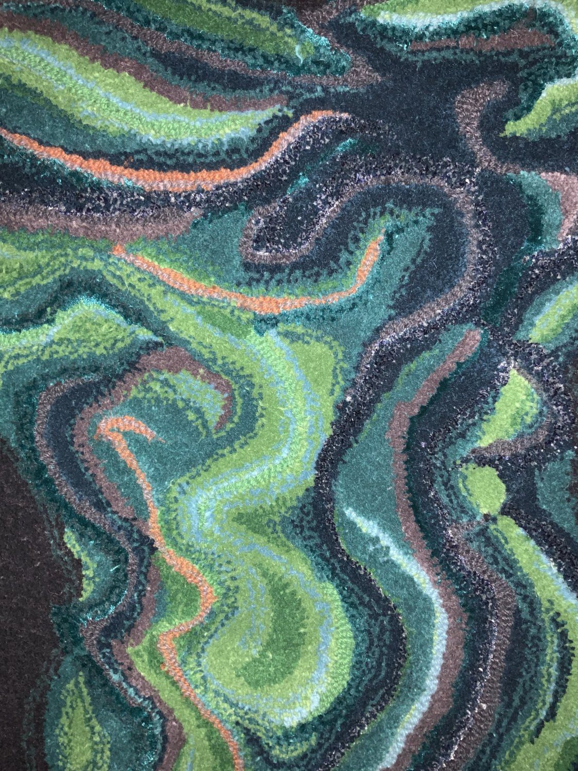 Close-up of a textured, abstract patterned tufted textile with swirling designs in shades of green, black, and orange.