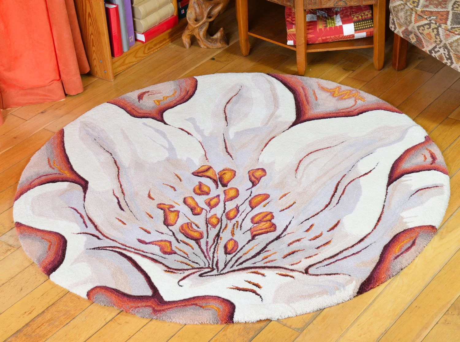 Oval area rug with a floral lily design in shades of cream, orange, yellow, and brown on a wooden floor in a cozy room.