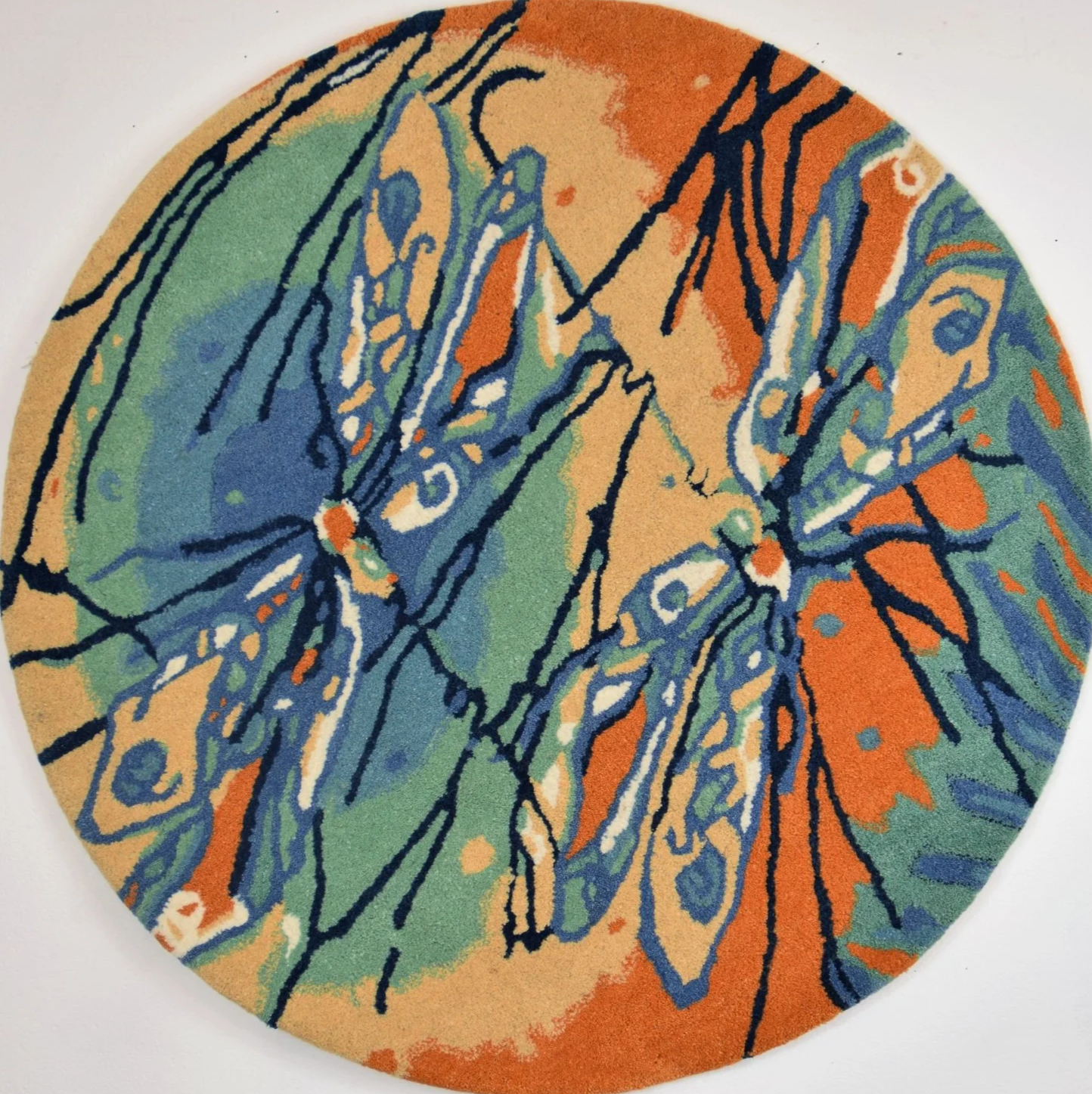 Colorful round rug featuring abstract dragonfly design with orange, green, blue, and white colors outlined in black.
