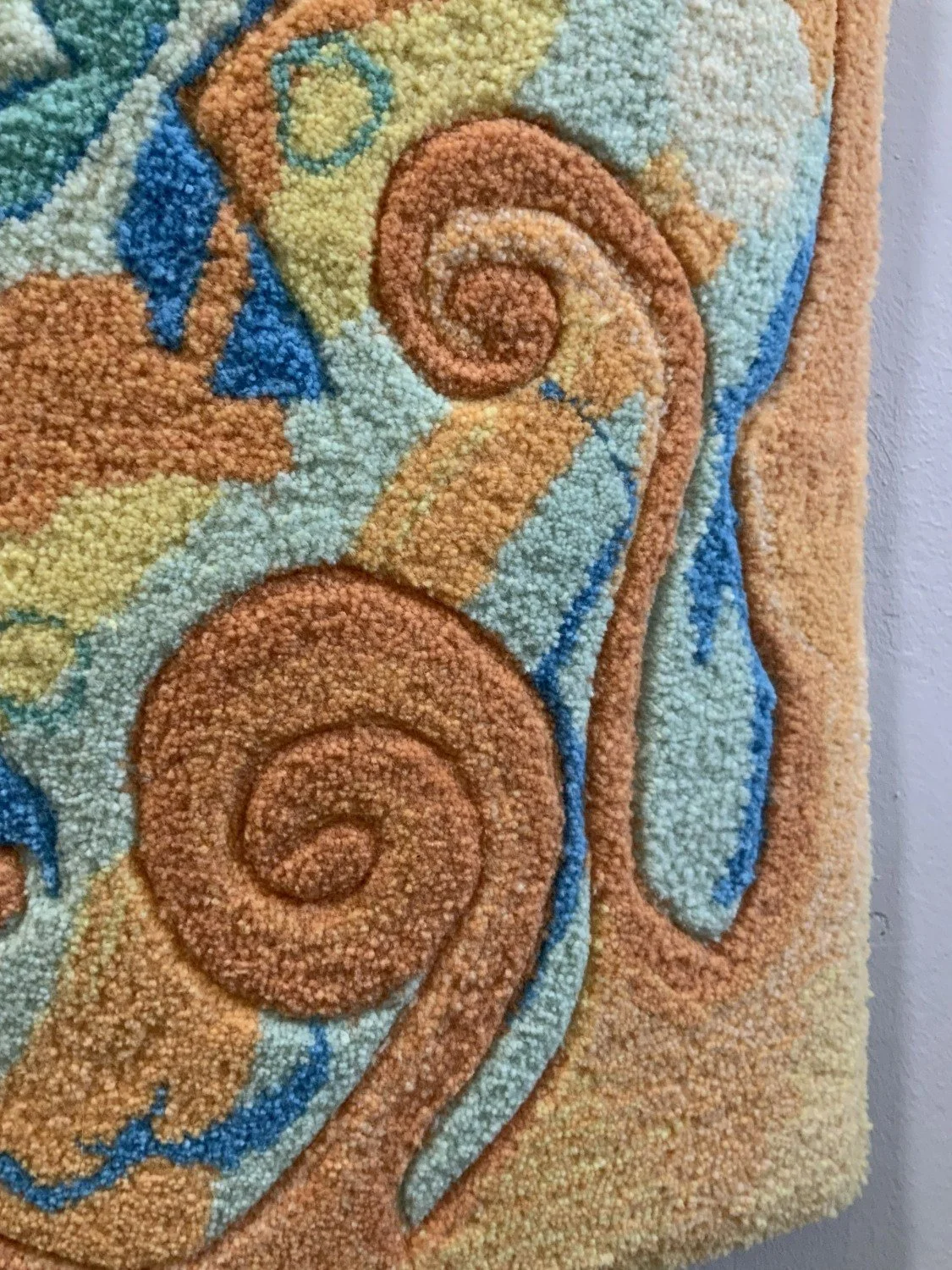 Close-up of a textured, multicolored rug with swirling patterns in shades of orange, blue, yellow, and cream.