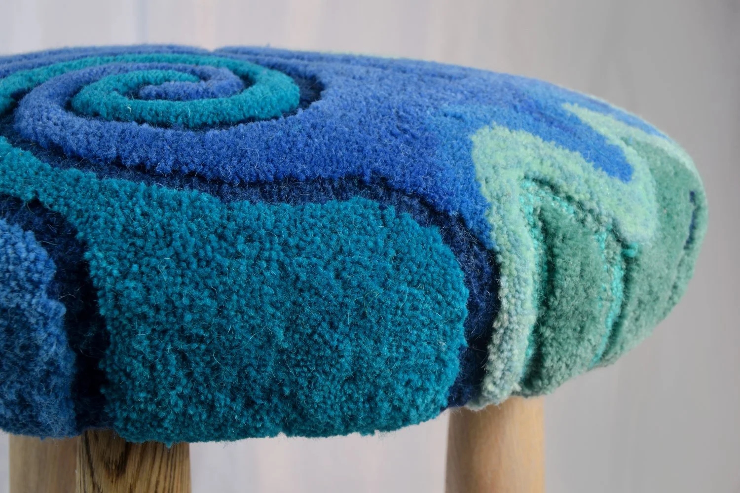 Close-up of a colorful, rolled-up, textured fabric stool with wooden legs.