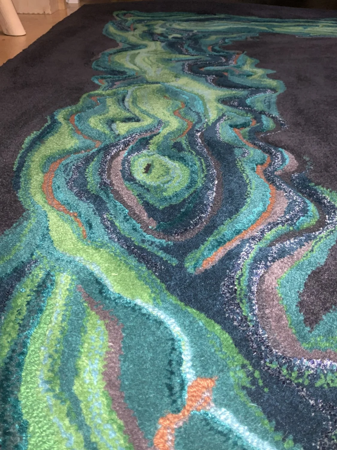Close-up of a colorful, abstract rug with swirling green, blue, and orange patterns on a dark background.