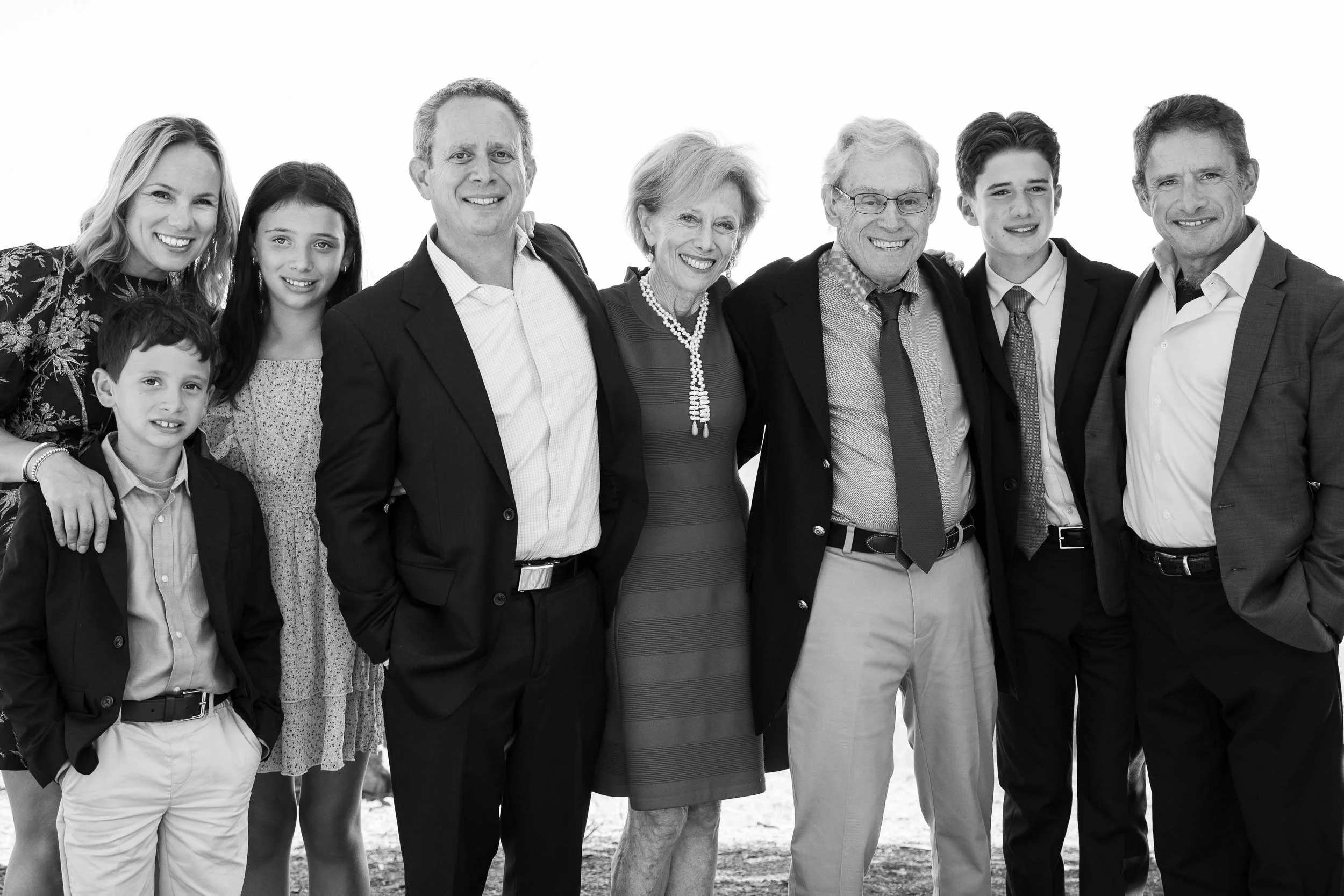 A family gathering with adults and children posing together outdoors, smiling in black and white photograph.