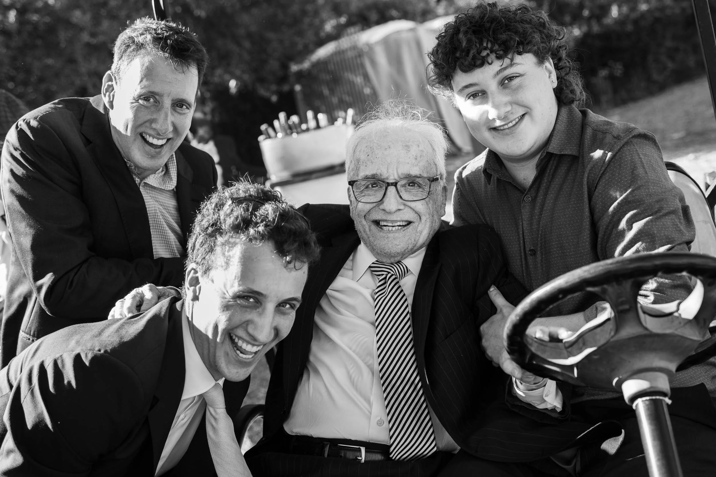 Five men in business attire smiling and gathered around a golf cart outdoors.