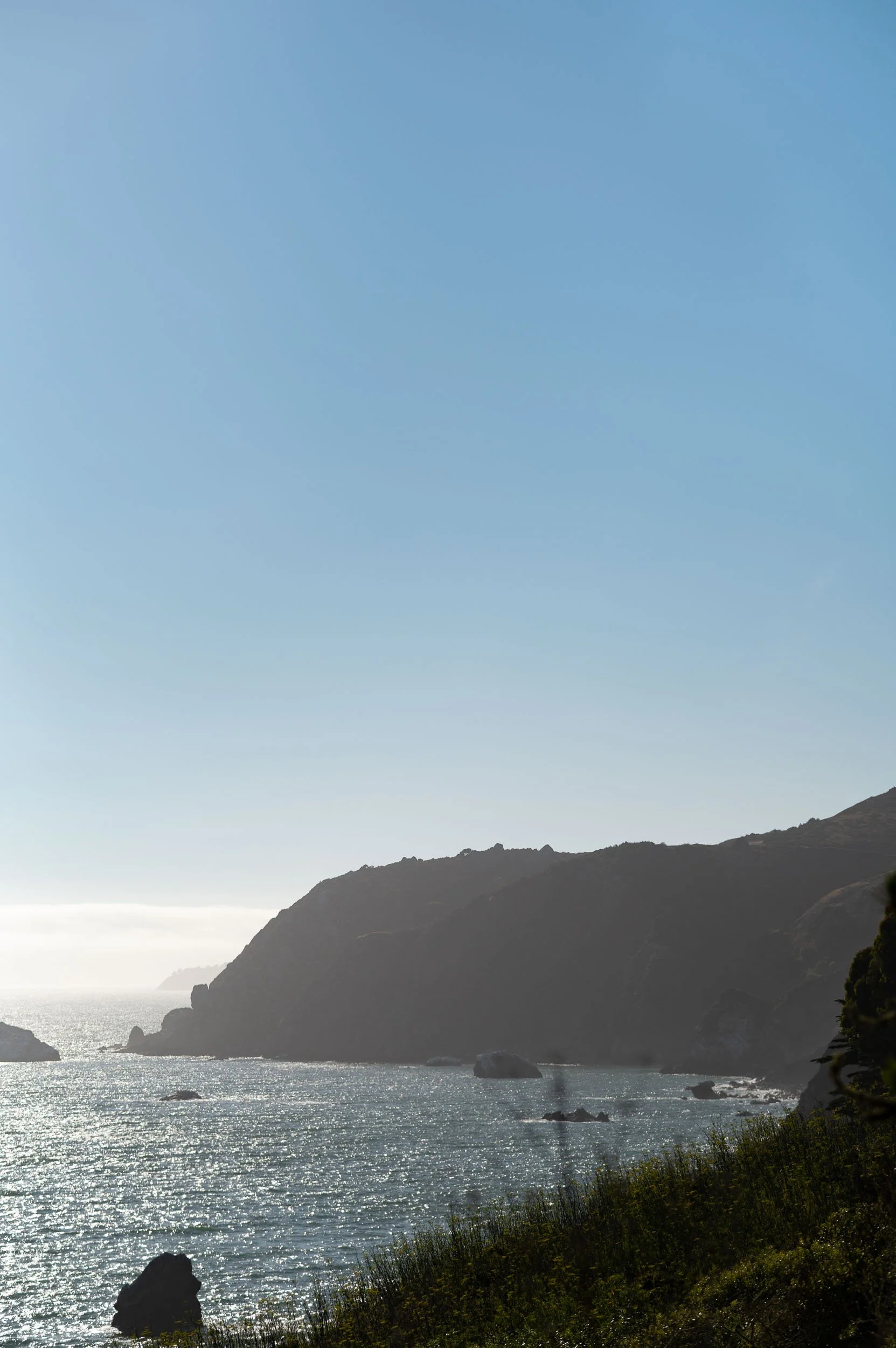 Scenic view of a coastal landscape with cliffs, rocks in the water, and clear blue sky.