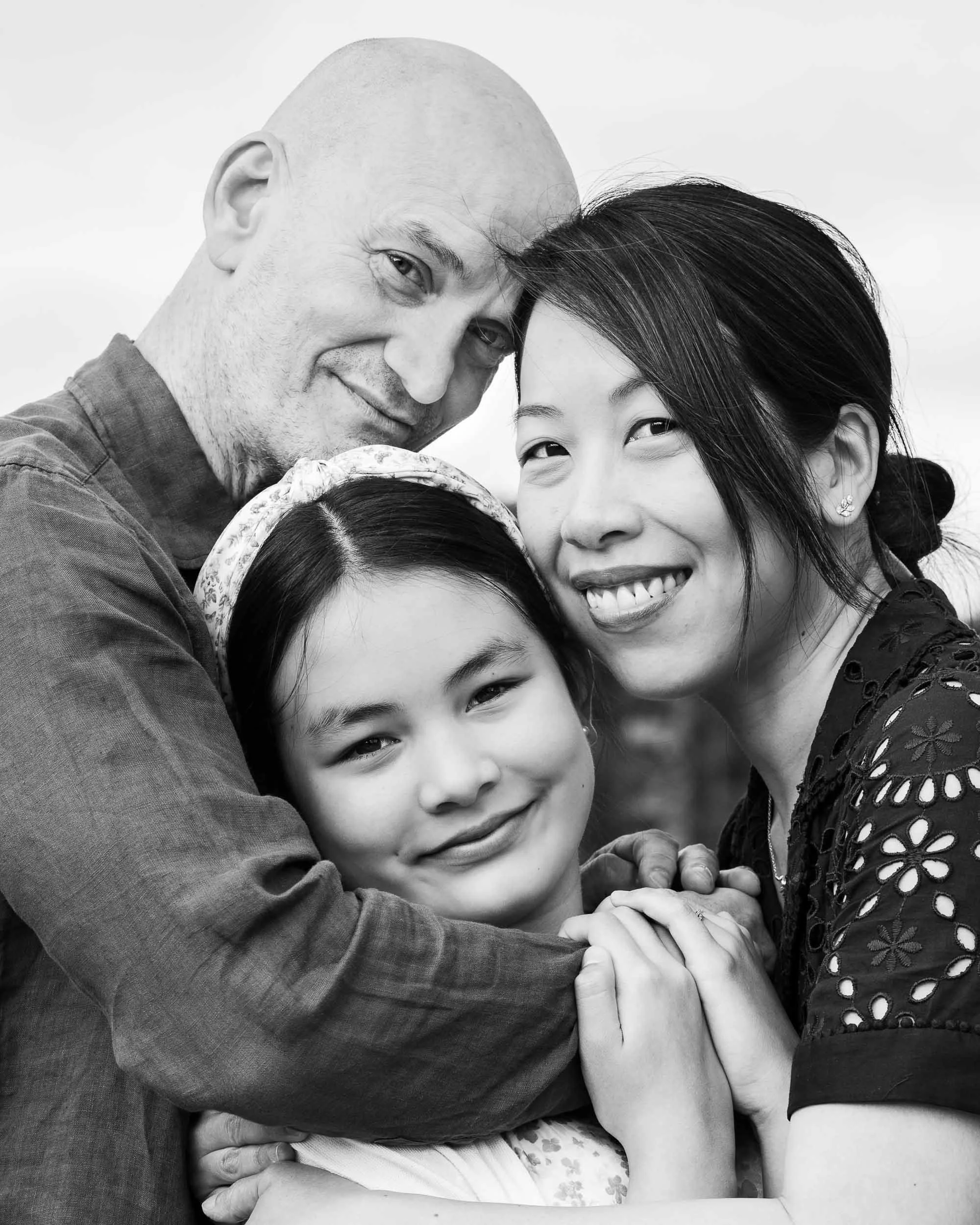 A black and white photo of a diverse group of people in a close embrace, showing happiness and affection.