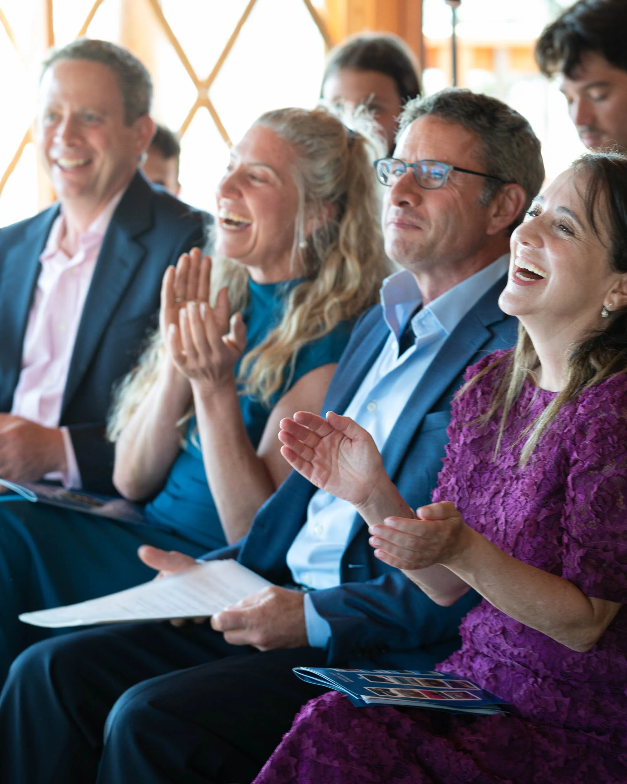 Group of people sitting and laughing at a conference or seminar, some clapping and smiling.
