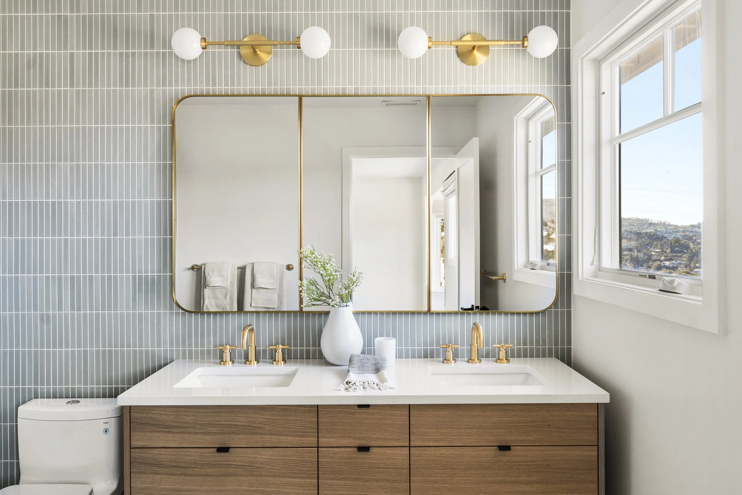 Primary bathroom renovation in Tiburon designed by Marin interior designer Studio SQUIRE featuring blue tile, wood vanity, brass plumbing fixtures, brass sconces, and brass mirror
