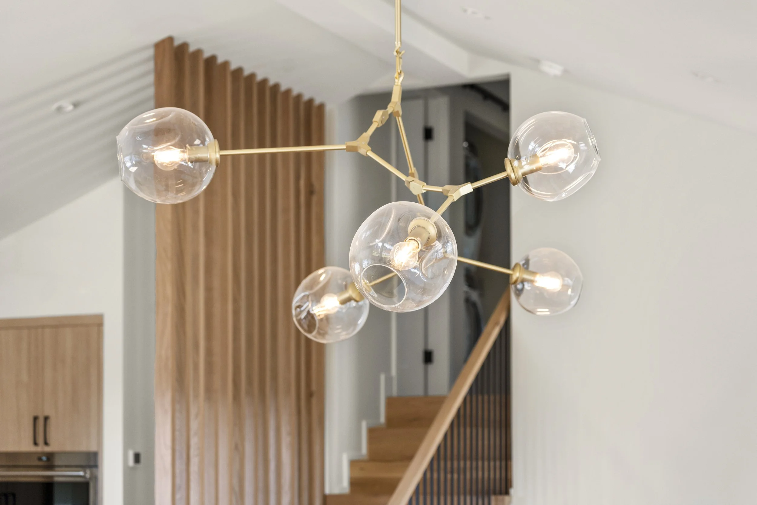 Whole home renovation in Tiburon designed by Marin interior designer Studio SQUIRE featuring modern white oak screen at stairs and modern branch chandelier.