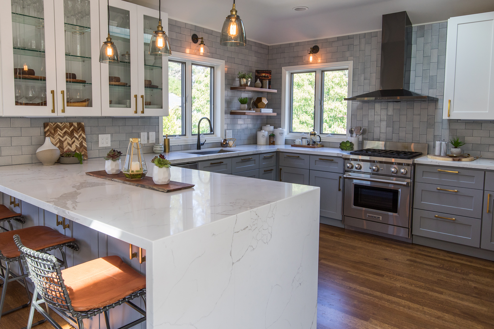 Kitchen renovation in Mill Valley designed by Marin interior designer Studio SQUIRE featuring Quartz Waterfall Island, Gray Cabinets, White Cabinets, Brass Hardware, Glass Pendants, and Subway Tile Backsplash
