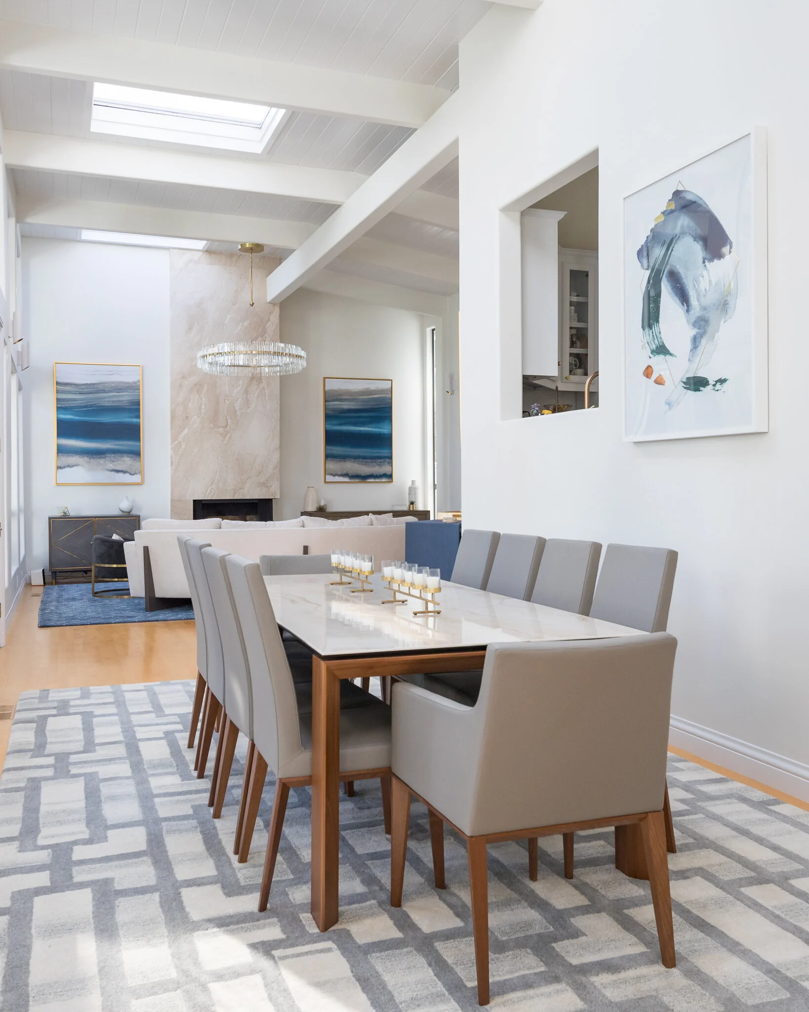 Dining room in a Mill Valley home designed by Marin interior designer Studio SQUIRE featuring a modern dining room table and chairs, modern art, floor to ceiling stone fireplace, and gray, blue and brass accents.
