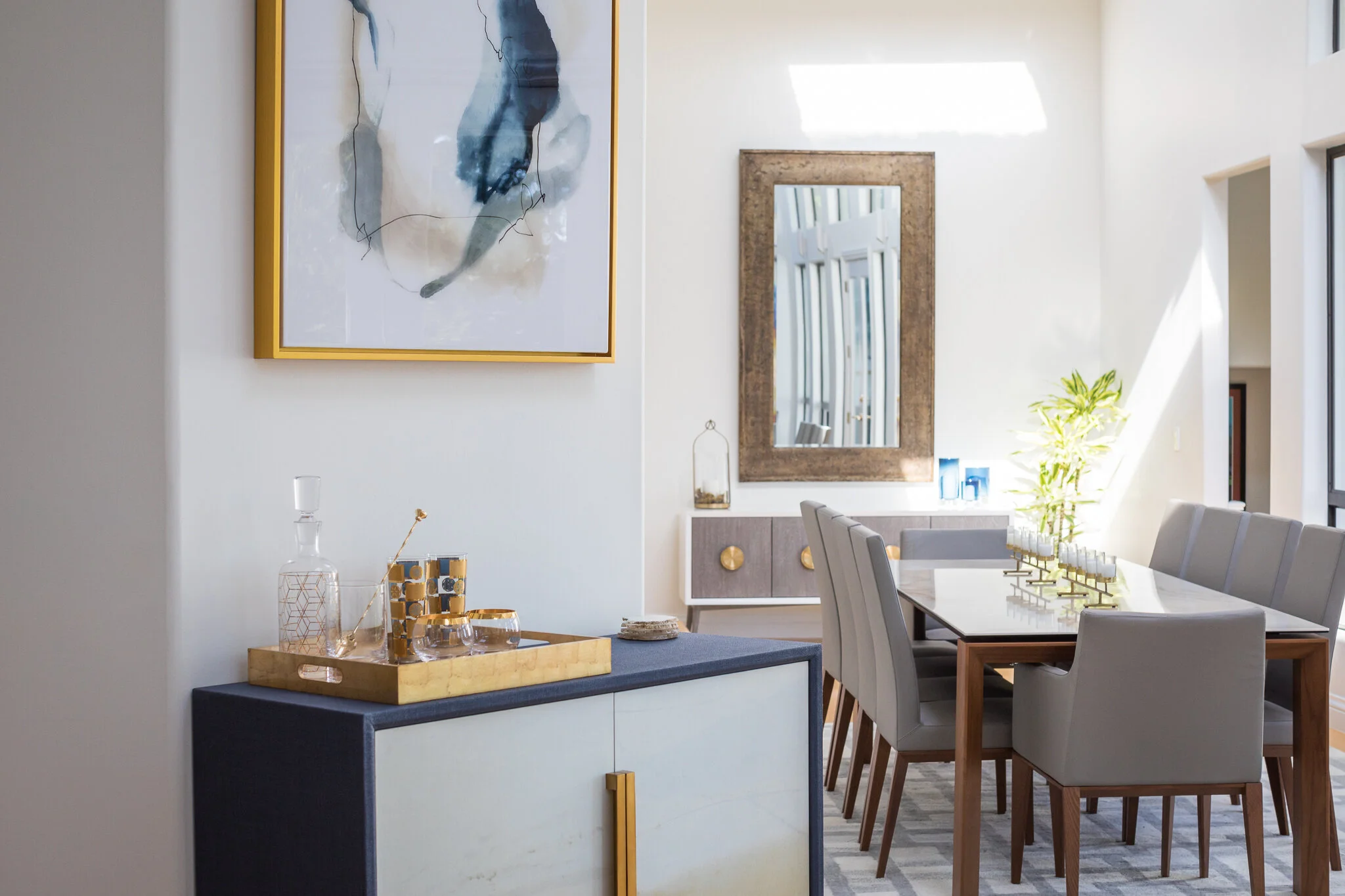 Dining room in a Mill Valley home designed by Marin interior designer Studio SQUIRE featuring a modern dining room table and chairs, modern art, a blue bar cabinet, and gray, blue and brass accents.
