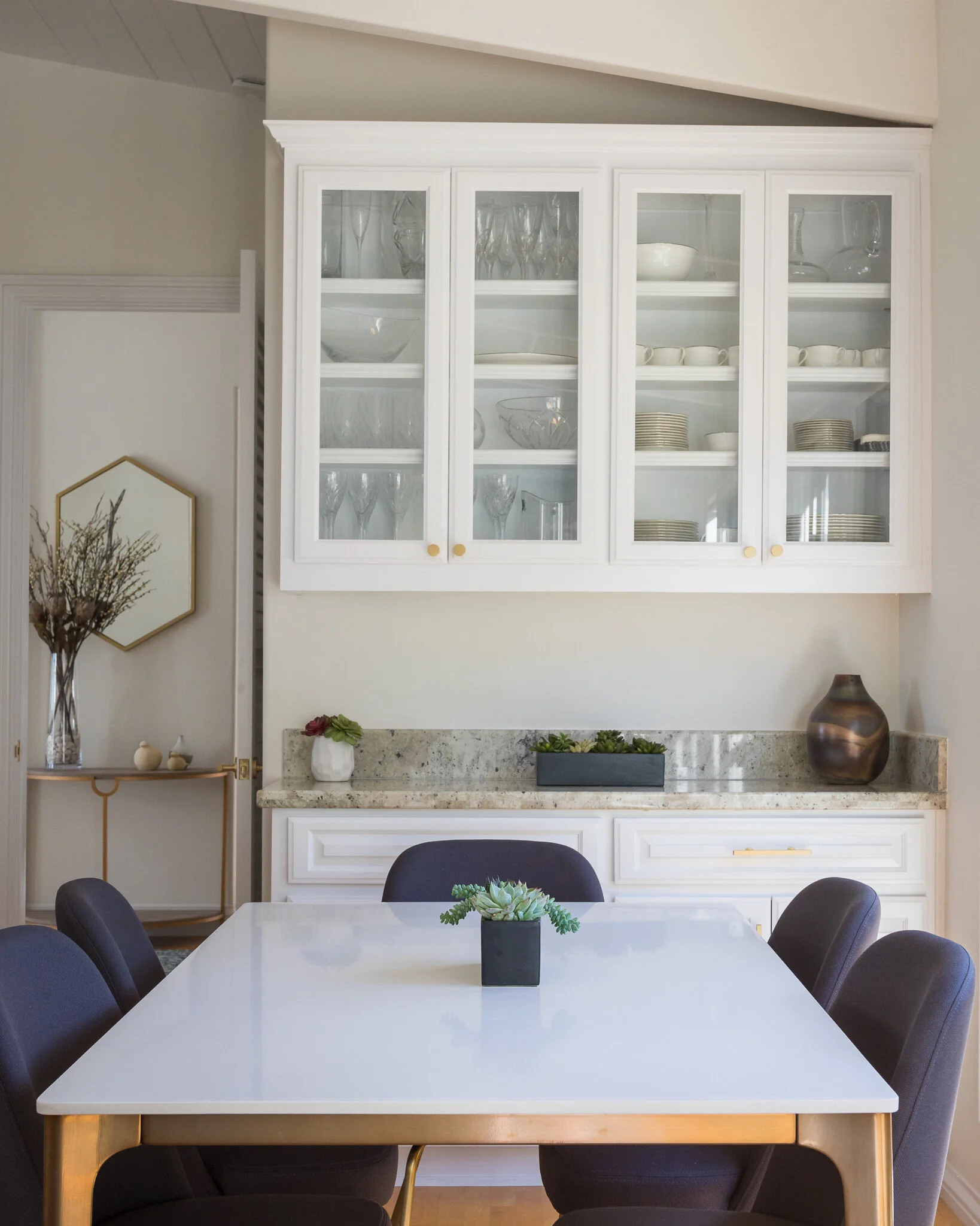 Breakfast nook in a Mill Valley home designed by Marin interior designer Studio SQUIRE featuring a modern table and chairs, stone countertops, brass hardware and accents, and succulents.
