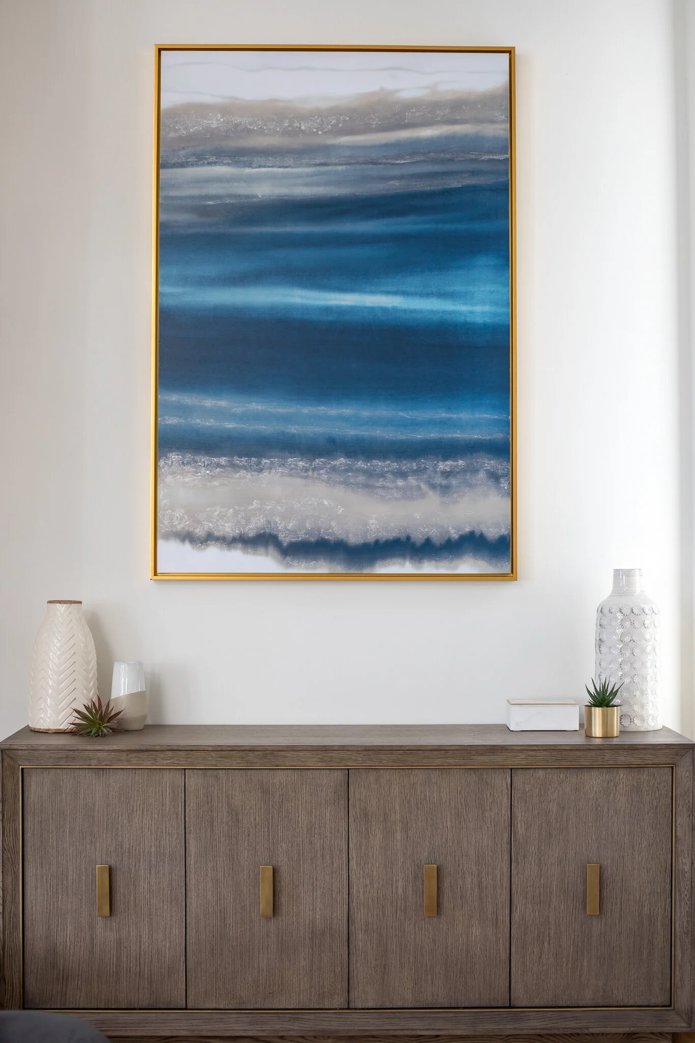 Living room in a Mill Valley home designed by Marin interior designer Studio SQUIRE featuring coastal inspired modern art above a gray wood sideboard.