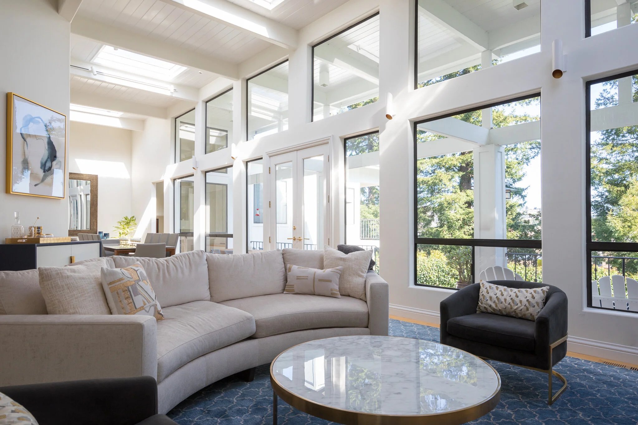 Living room in a Mill Valley home designed by Marin interior designer Studio SQUIRE featuring a statement chandelier, curved sofa, modern art, floor to ceiling stone fireplace, and brass accents.