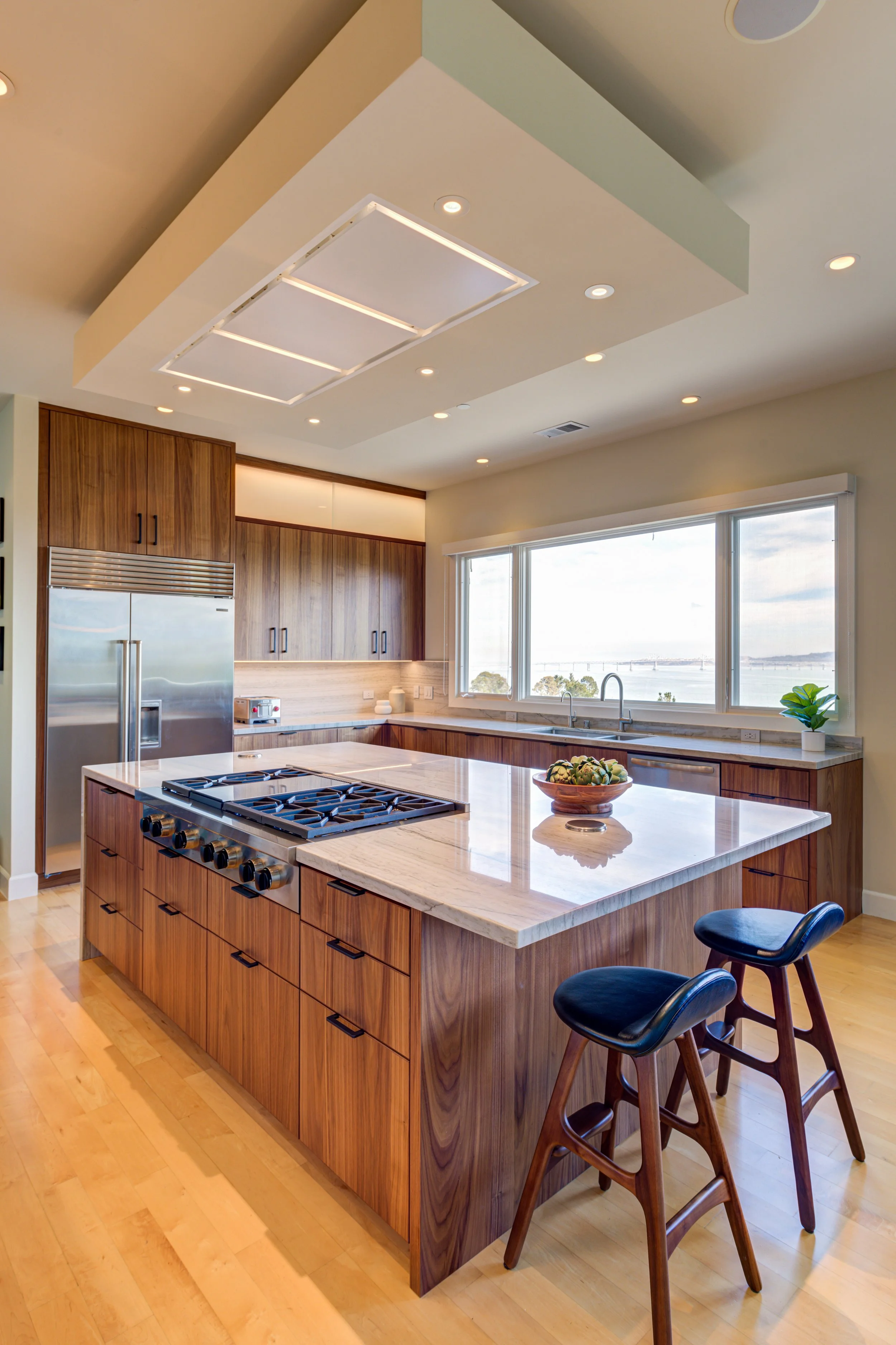 Luxury kitchen renovation in Belvedere-Tiburon designed by Marin interior designer Studio SQUIRE featuring walnut cabinets, matte black, cabinet hardware, quartzite countertops, Subzero Wolf appliances, and panoramic views of the San Francisco Bay.