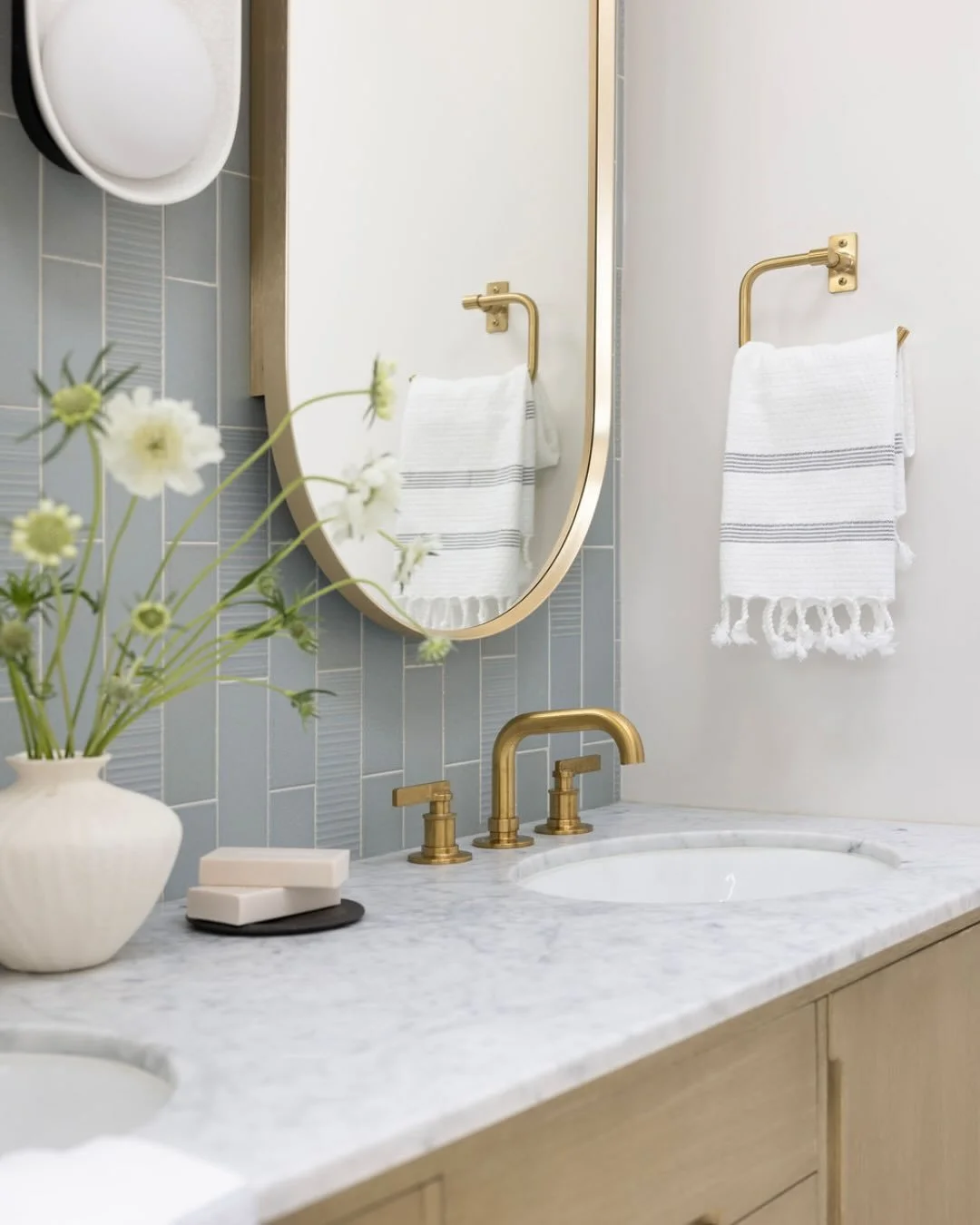 Some spaces invite you to slow down the moment you step inside.

Designed with a soft, coastal palette, this bathroom layers gentle blue tile, warm oak cabinetry, honed stone, brushed brass fixtures, and natural light to create a retreat that feels c