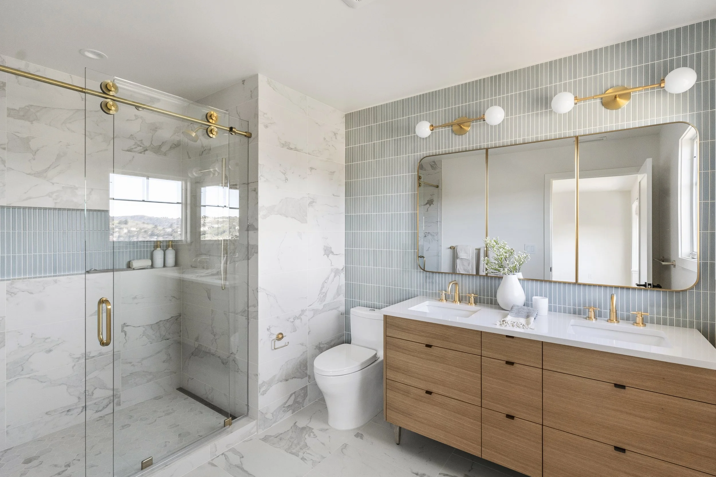 Primary bathroom renovation in Tiburon designed by Marin interior designer Studio SQUIRE featuring marble tile, blue tile, wood vanity, and brass fixtures