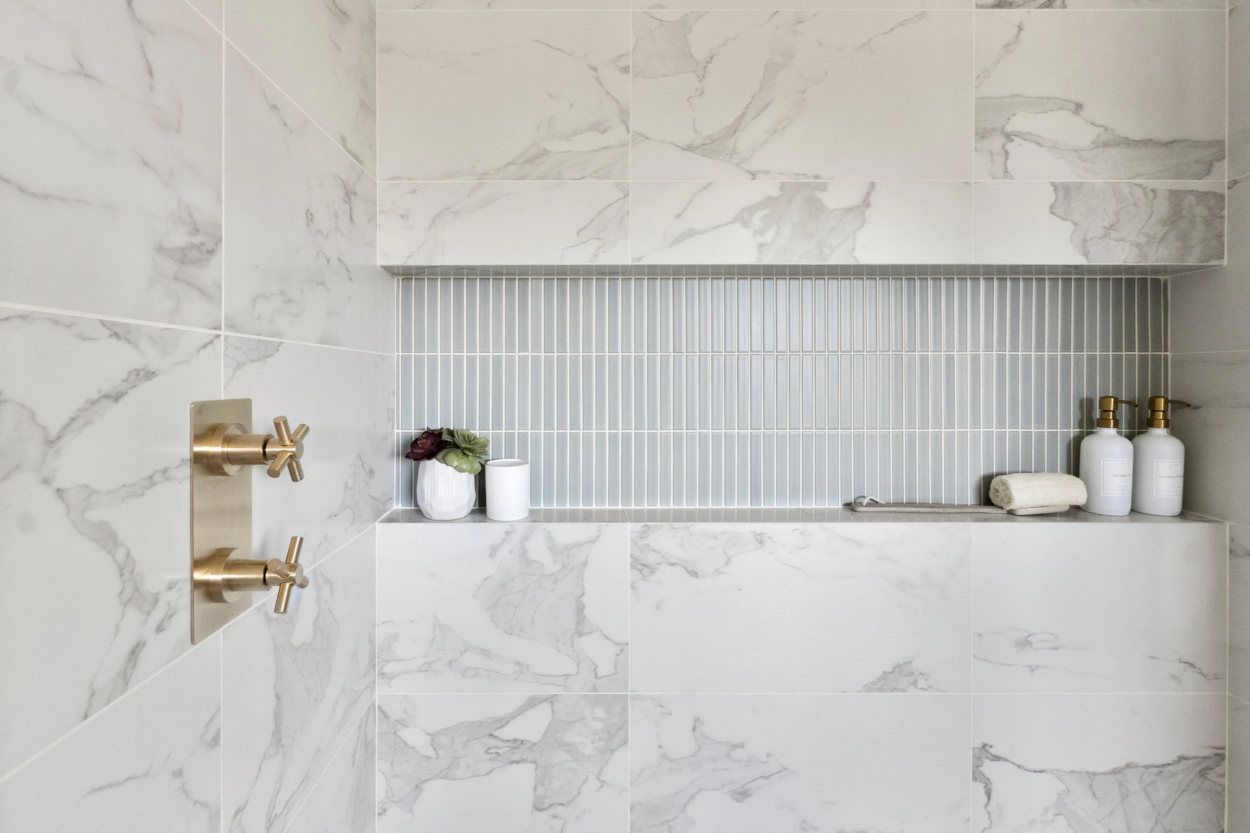 Primary bathroom renovation in a Tiburon home designed by Marin interior designer Studio SQUIRE featuring blue tile, marble tile, brass plumbing fixtures, and a wall-to-wall modern shower niche.