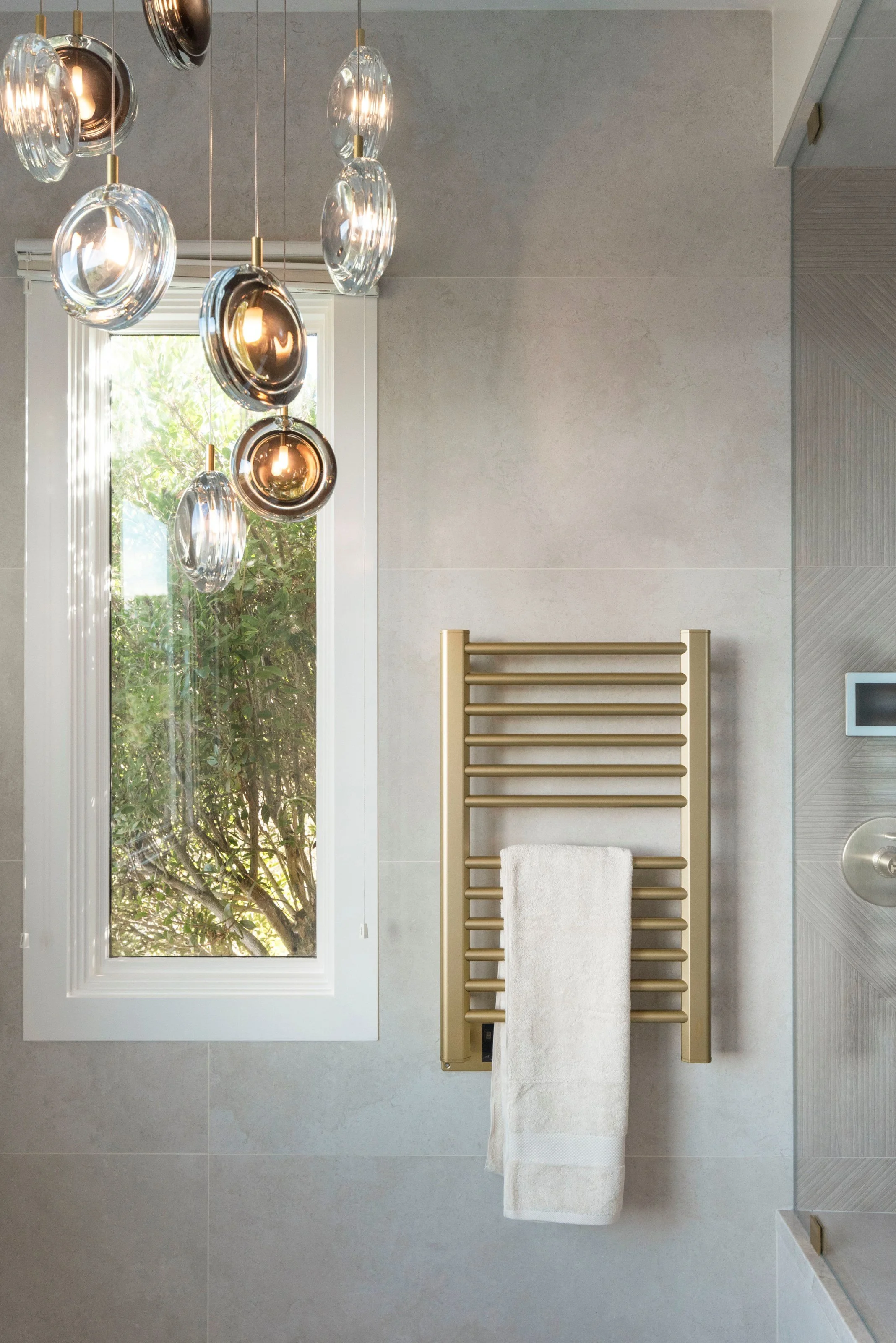 Luxury primary bathroom renovation in Tiburon designed by Marin interior designer Studio SQUIRE featuring a coastal modern design, satin brass towel warmer, and modern chandelier.