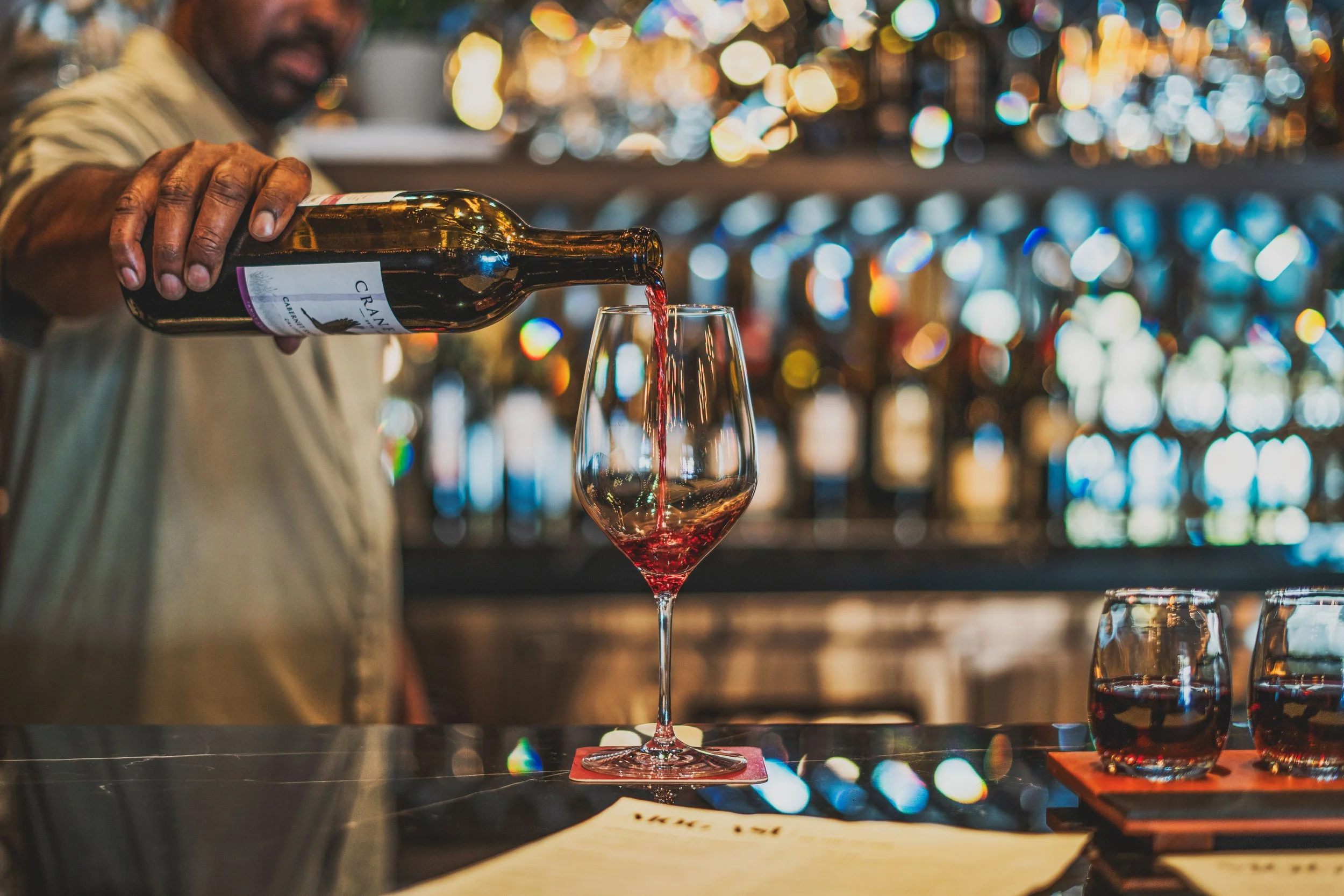 Commercial wine bar renovation in Belvedere-Tiburon designed by Marin interior designer Studio SQUIRE featuring a Black Marble Countertop, Mirrored Backsplash, and Wood Shelves