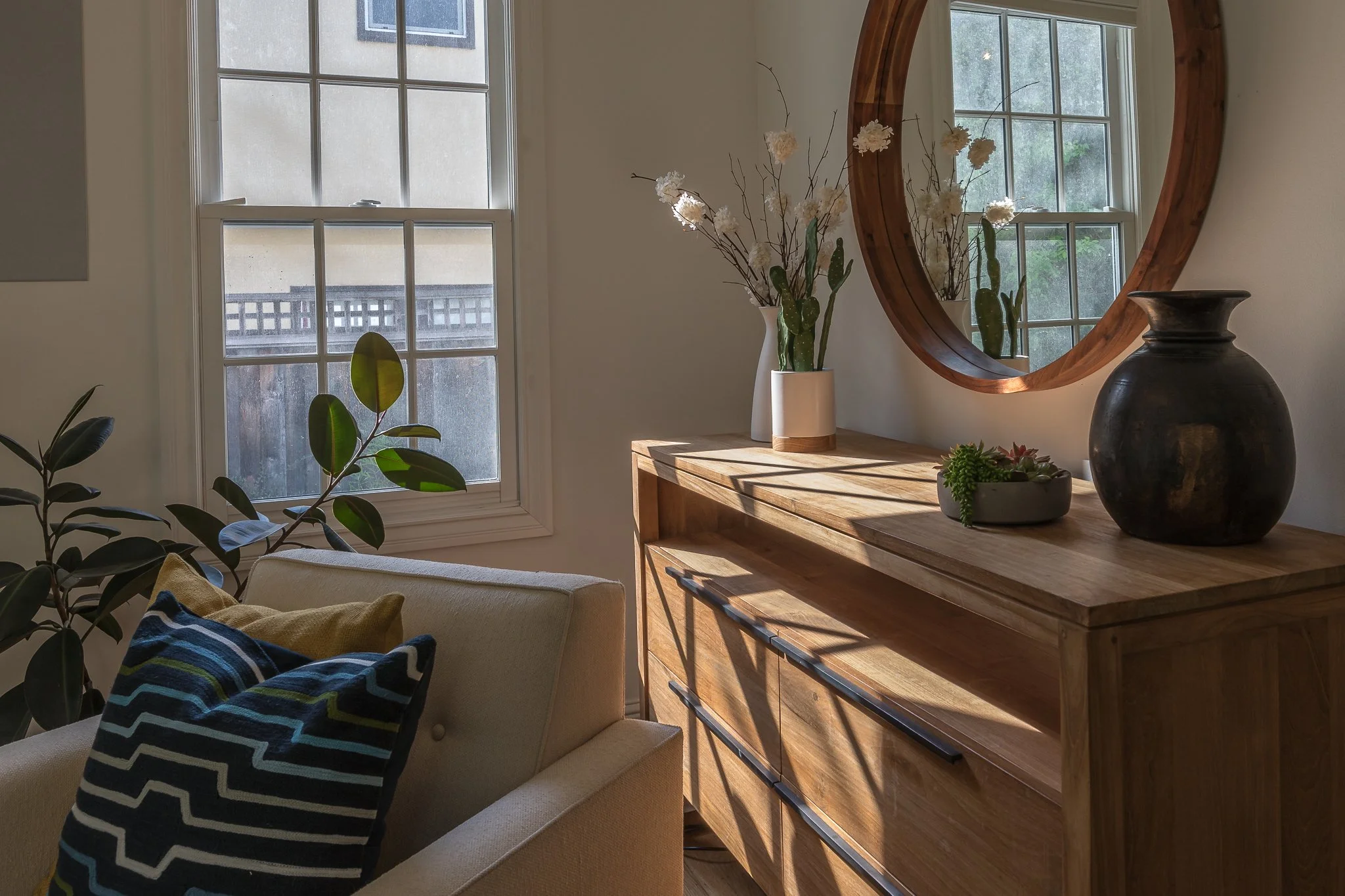 Living room in a San Rafael home designed by Marin interior designer Studio SQUIRE featuring modern wood furniture, a large round mirror, and comfortable furniture.