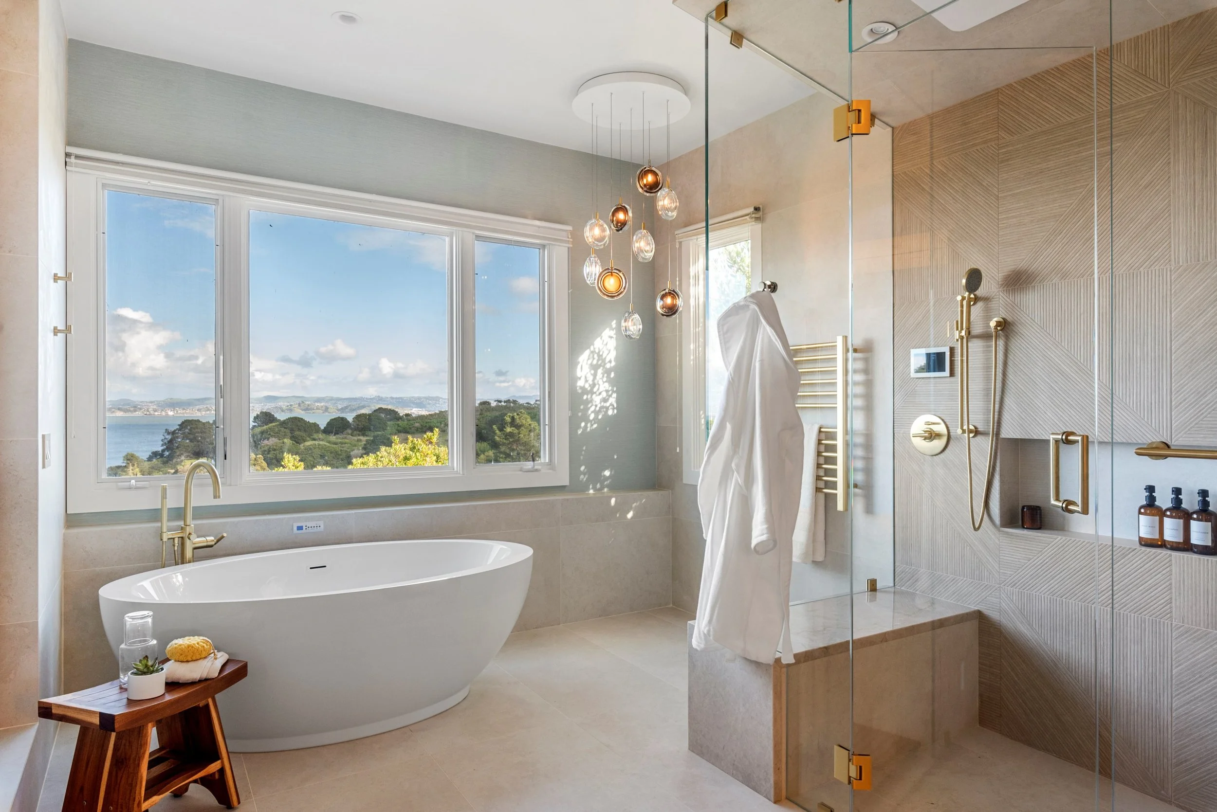 Primary bathroom renovation in Belvedere-Tiburon designed by Marin interior designer Studio SQUIRE featuring a hydrotherapy soaking tub, custom steam shower, towel warmer, modern lighting fixtures, and views of the San Francisco Bay.
