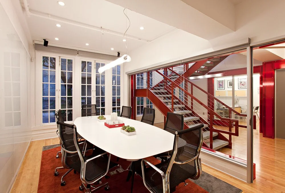 Commercial Office renovation in San Francisco designed by Marin interior designer Studio SQUIRE featuring a white conference table, black chairs, red staircase and wall trim