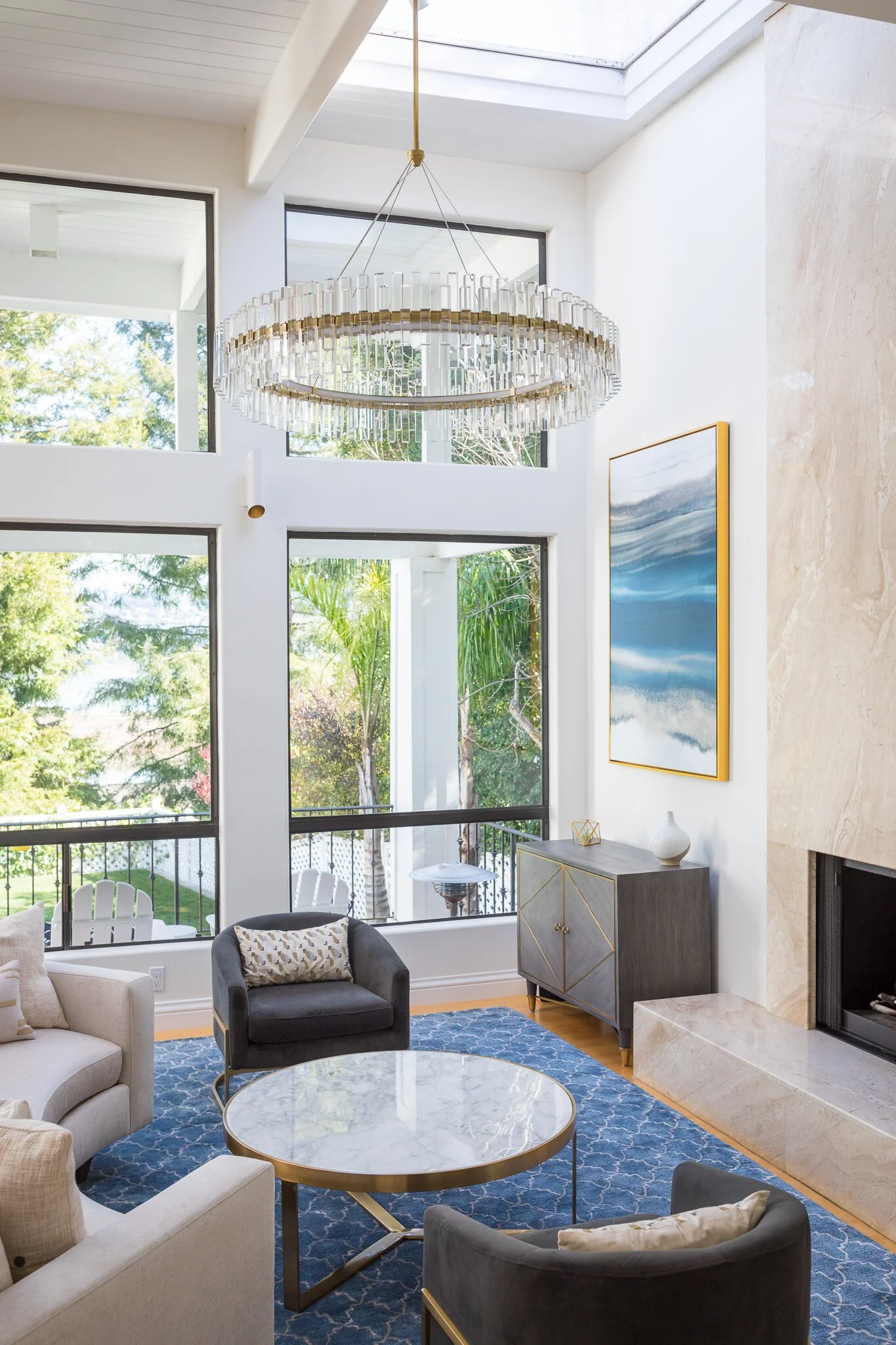 Living room in a Mill Valley home designed by Marin interior designer Studio SQUIRE featuring a statement chandelier, curved sofa, modern art, floor to ceiling stone fireplace, and brass accents.