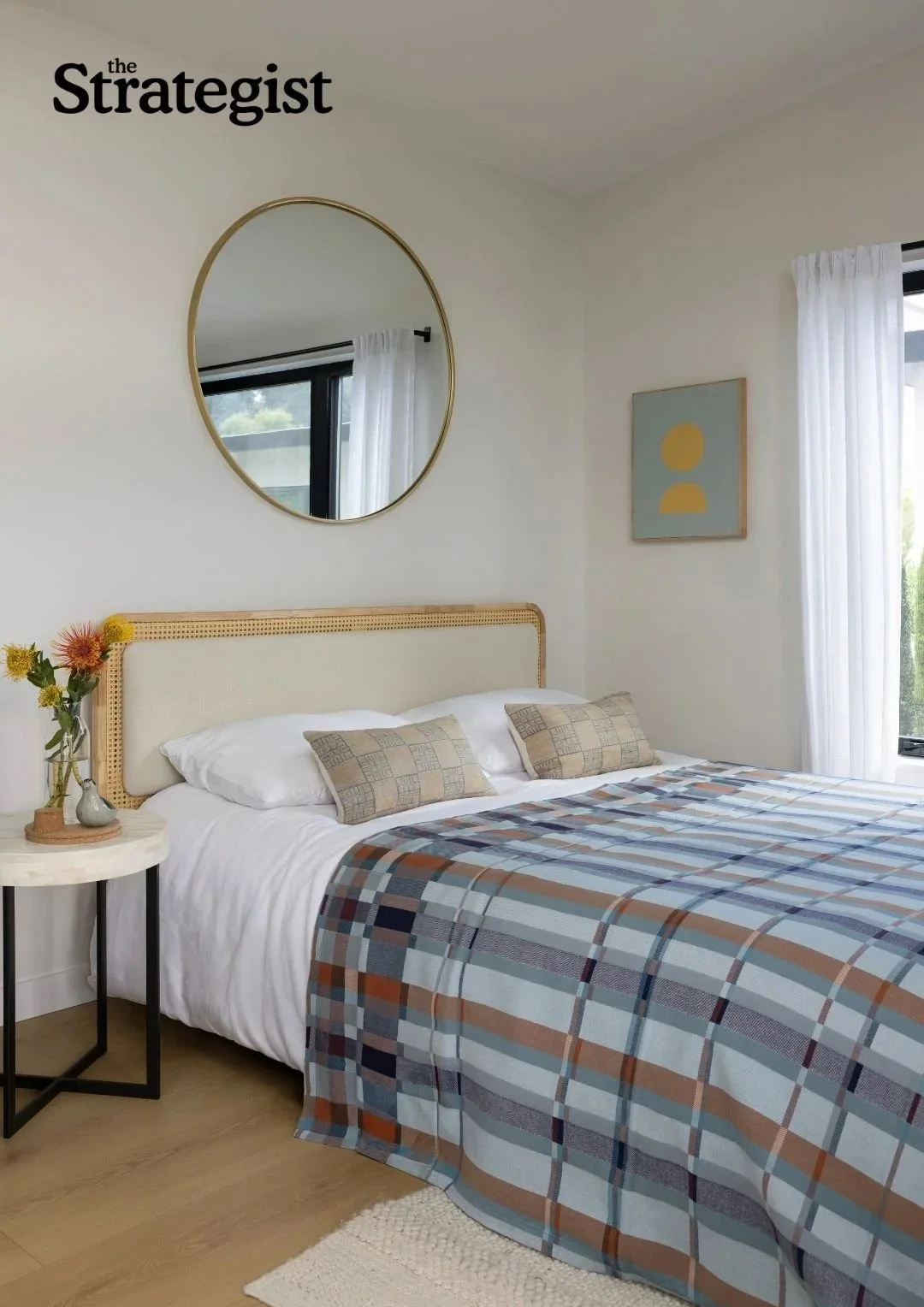 ADU renovation in Mill Valley designed by Marin interior designer Studio SQUIRE featuring rattan headboard, brass round mirror, accent pillows, plaid duvet, and side table